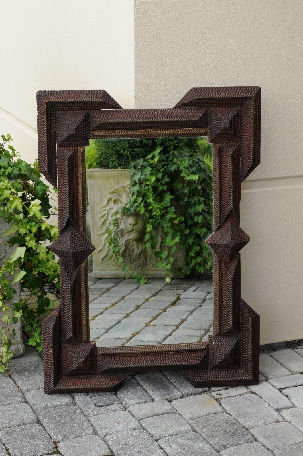 A French Tramp Art carved wood mirror from the early 20th century, with raised motifs, dark patina and protruding corners. Born in France during the turn of the century (19th to 20th), this French Tramp Art mirror features a linear frame with raised