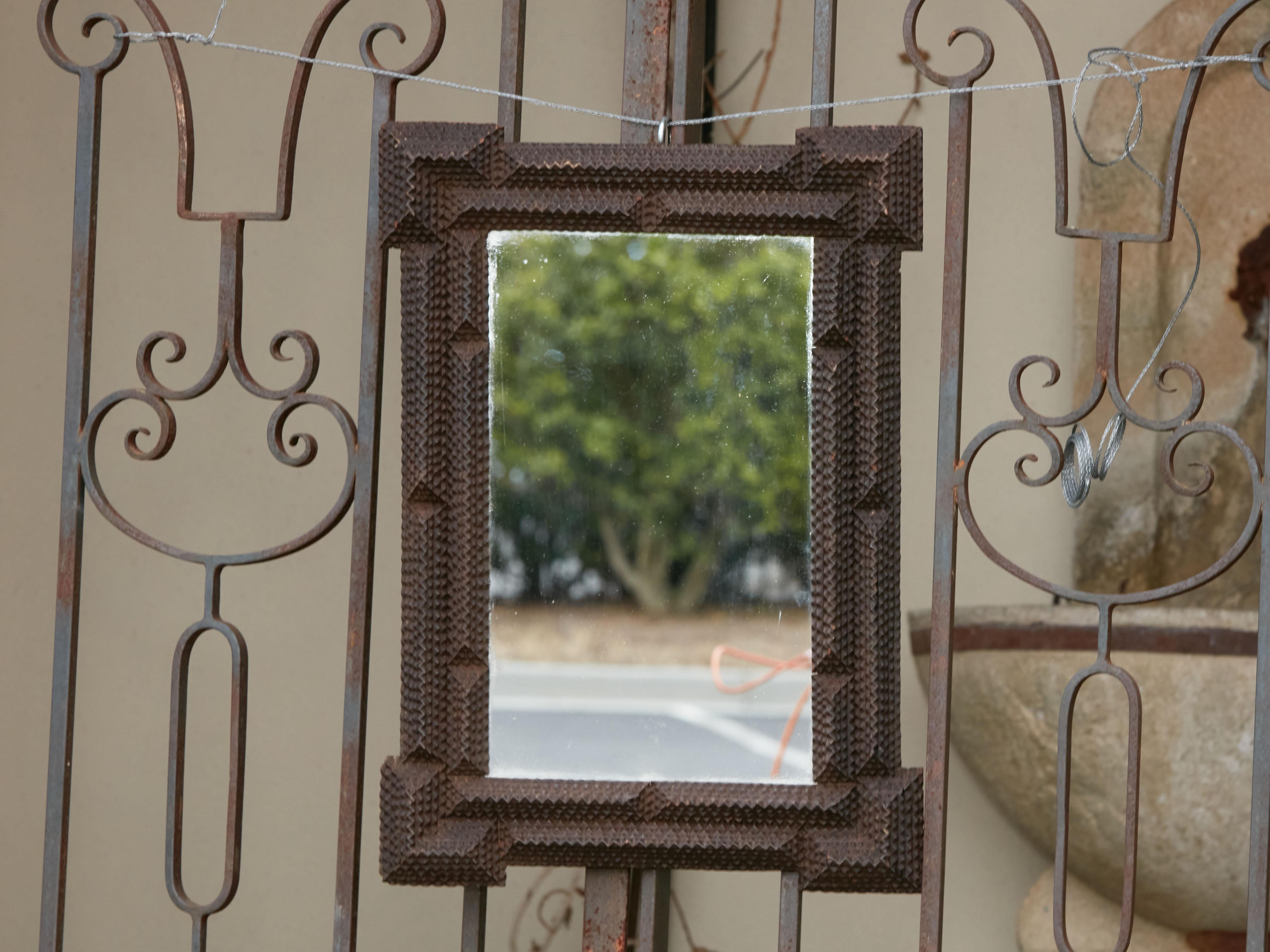 A small French Tramp Art hand carved wood mirror from the early 20th century, with raised motifs, dark patina and protruding corners. Created in France during the Turn of the Century which saw the transition between the 19th to the 20th, this wooden