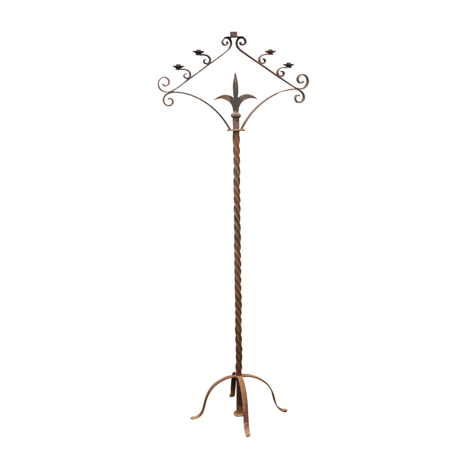 A tall French iron floor standing candelabra from the early 20th century, with five prickets, scrollwork design, stylized fleur de lys motif and twisted accents on a quadripartite base. Created in France at the Turn of the Century (19th to 20th