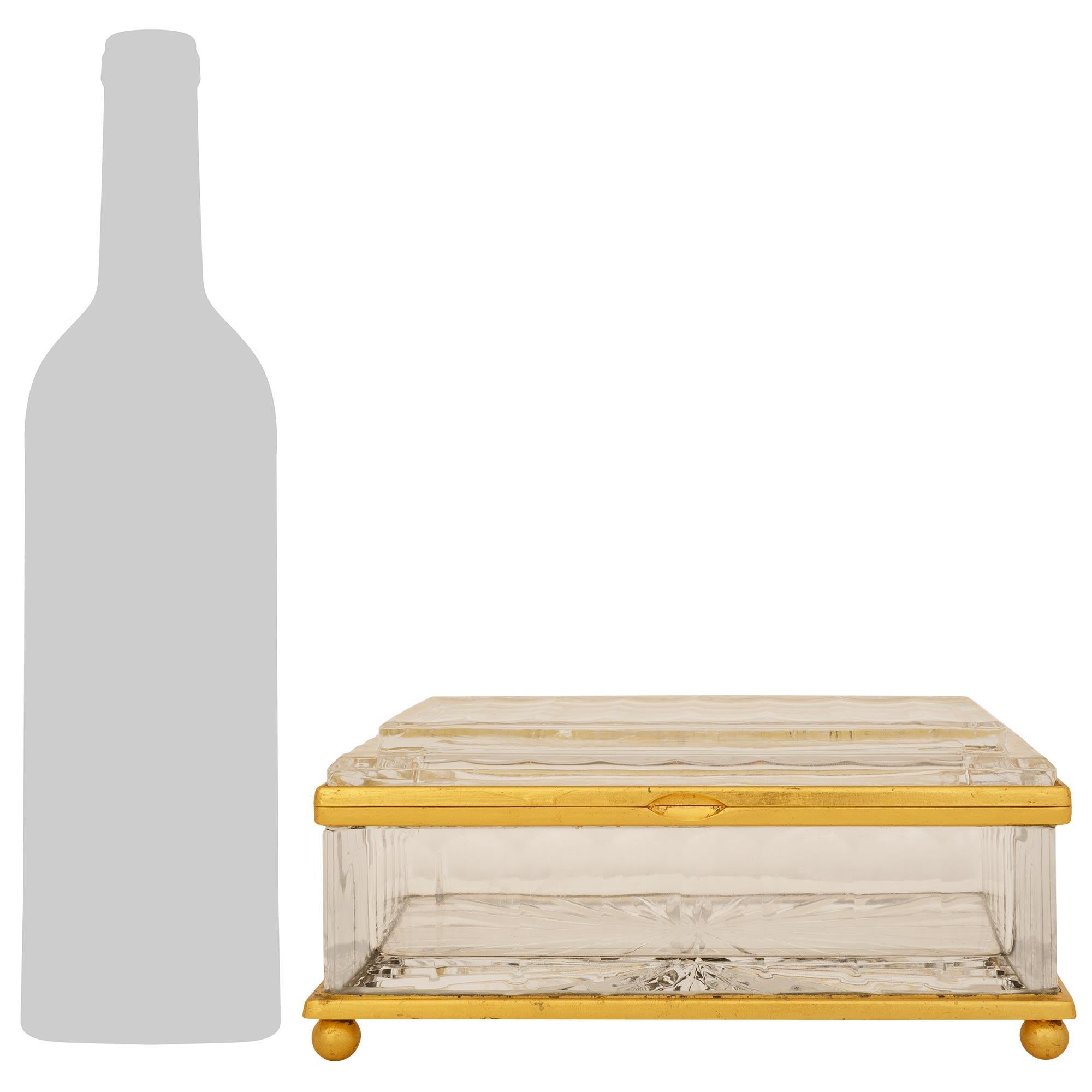 An elegant French Turn of the Century Louis XVI st. Crystal and Gilt Bronze box. This charming rectangular box is raised on ball feet below the bottom rectangular Gilt Bronze band. The underside displays a stunning cut sunburst design. The top rim