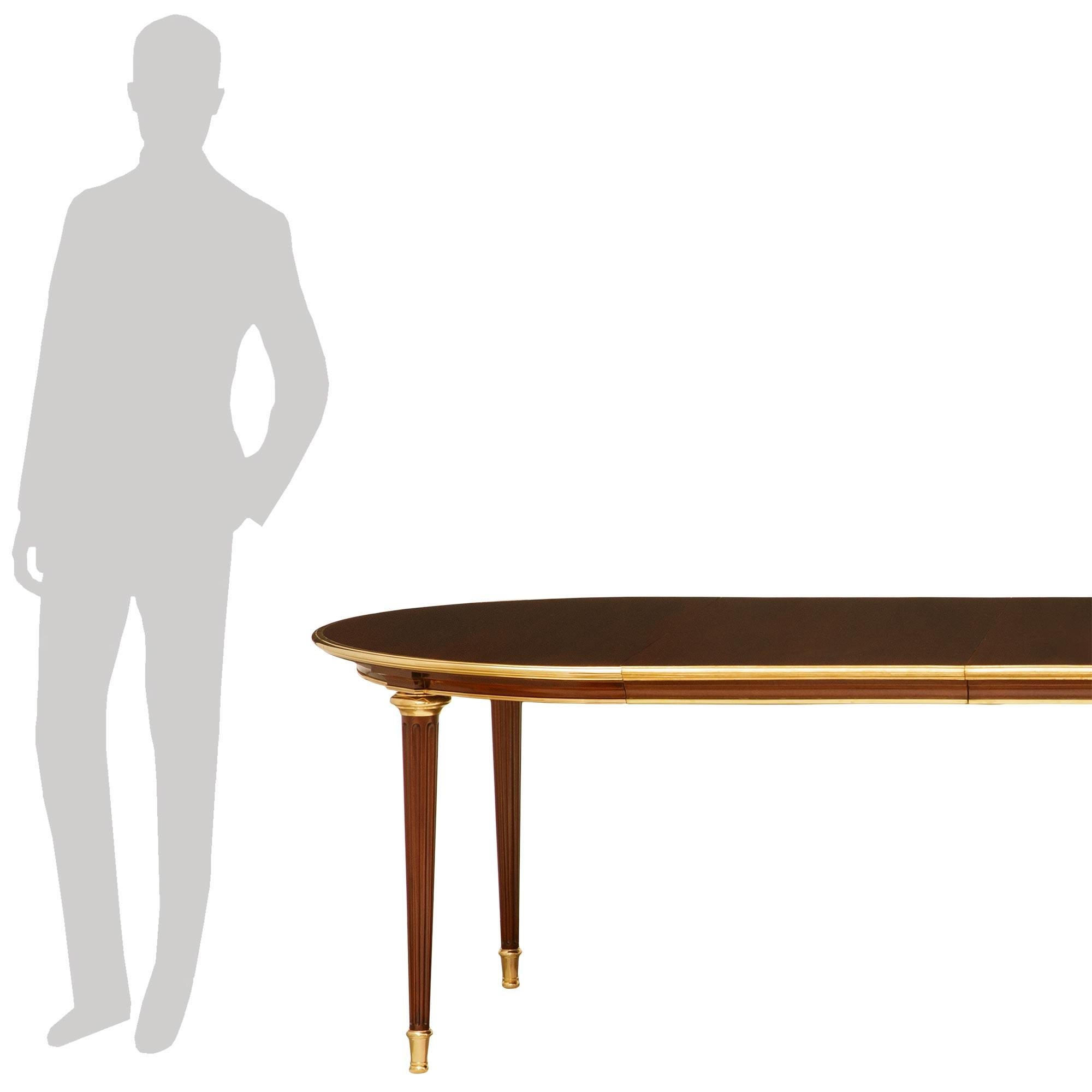 An elegant and high quality French Turn of the Century Louis XVI st. Mahogany and Ormolu dining table. This wonderful oval dining table with three extensions is raised on five circular tapered and fluted Mahogany legs with Ormolu sabots. The legs
