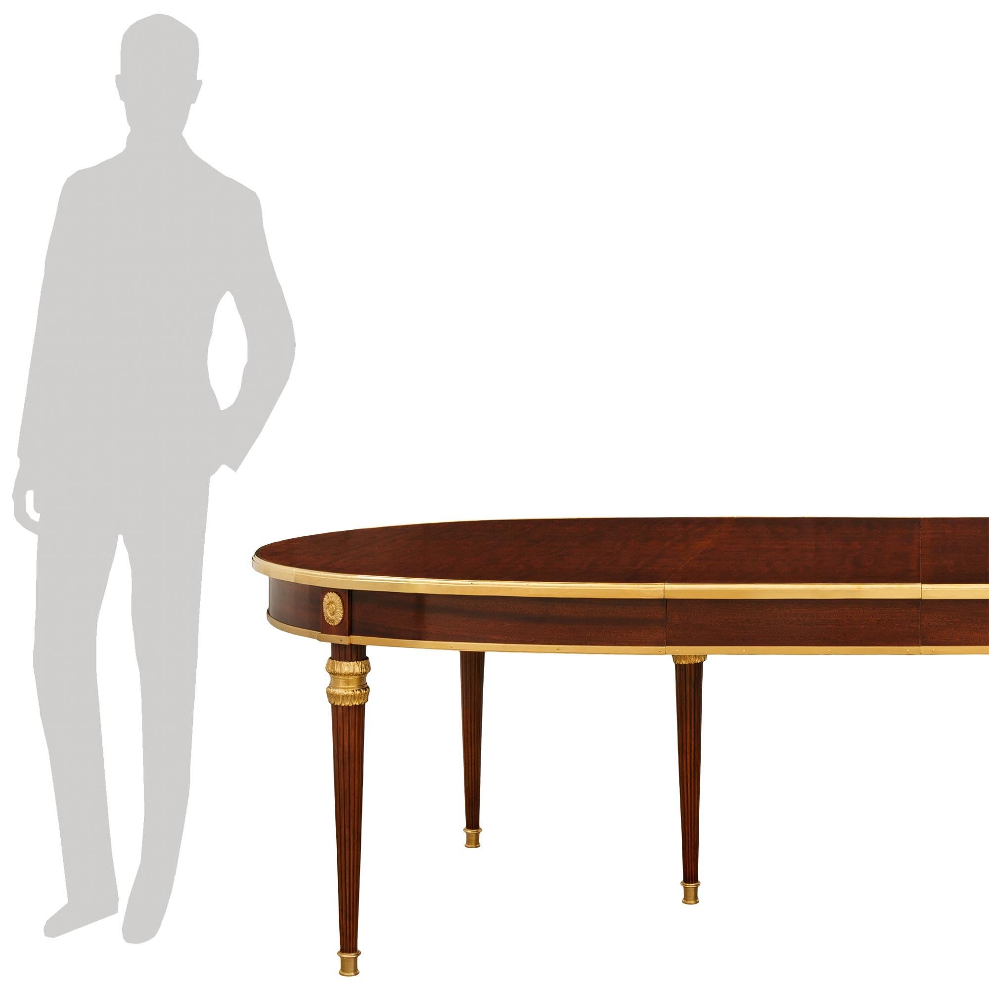 Superbe table de salle à manger en acajou et bronze doré de style Louis XVI du début du siècle, attribuée à la Maison Jansen. Cette exceptionnelle table ovale repose sur d'élégants pieds circulaires fuselés, dotés de sabots en bronze doré finement