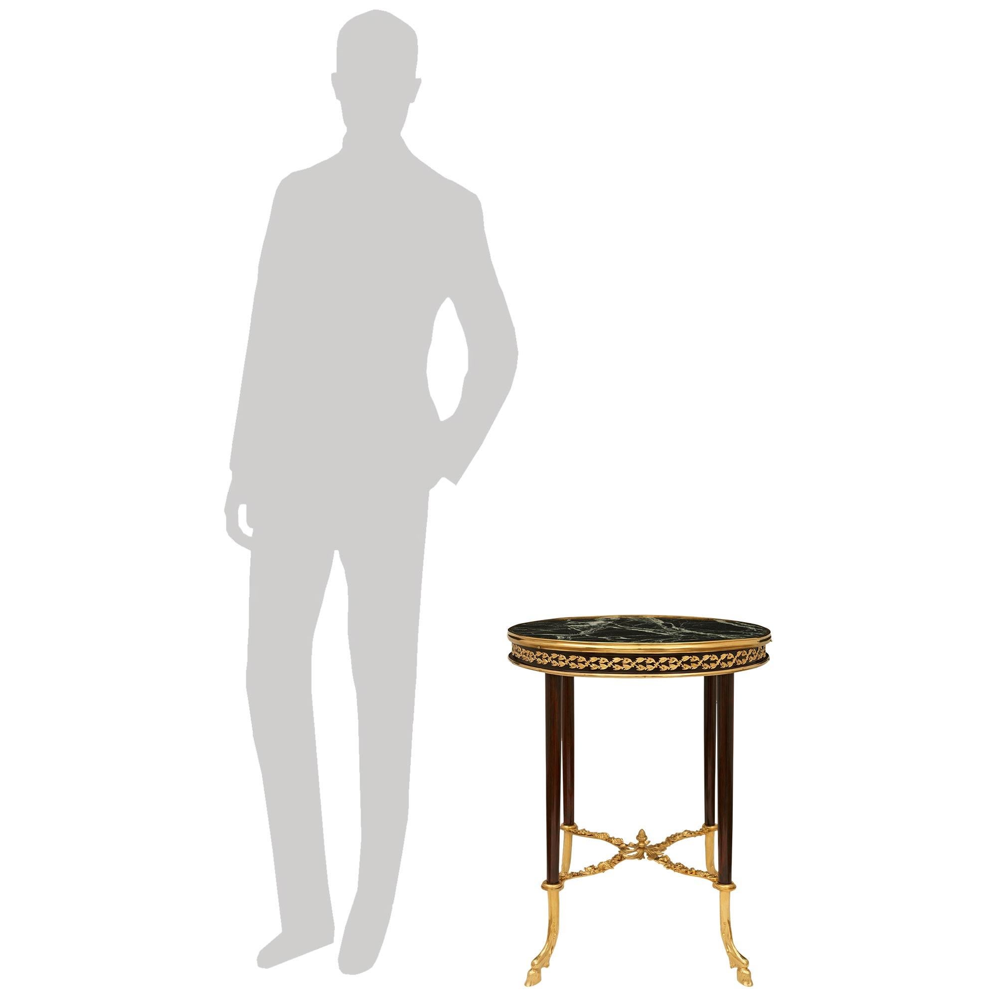 Table d'appoint élégante et très décorative de style Louis XVI en acajou, bronze doré et marbre Verde Alpi. Cette merveilleuse table circulaire repose sur quatre pieds circulaires effilés en acajou qui se terminent par des pieds fantaisistes en