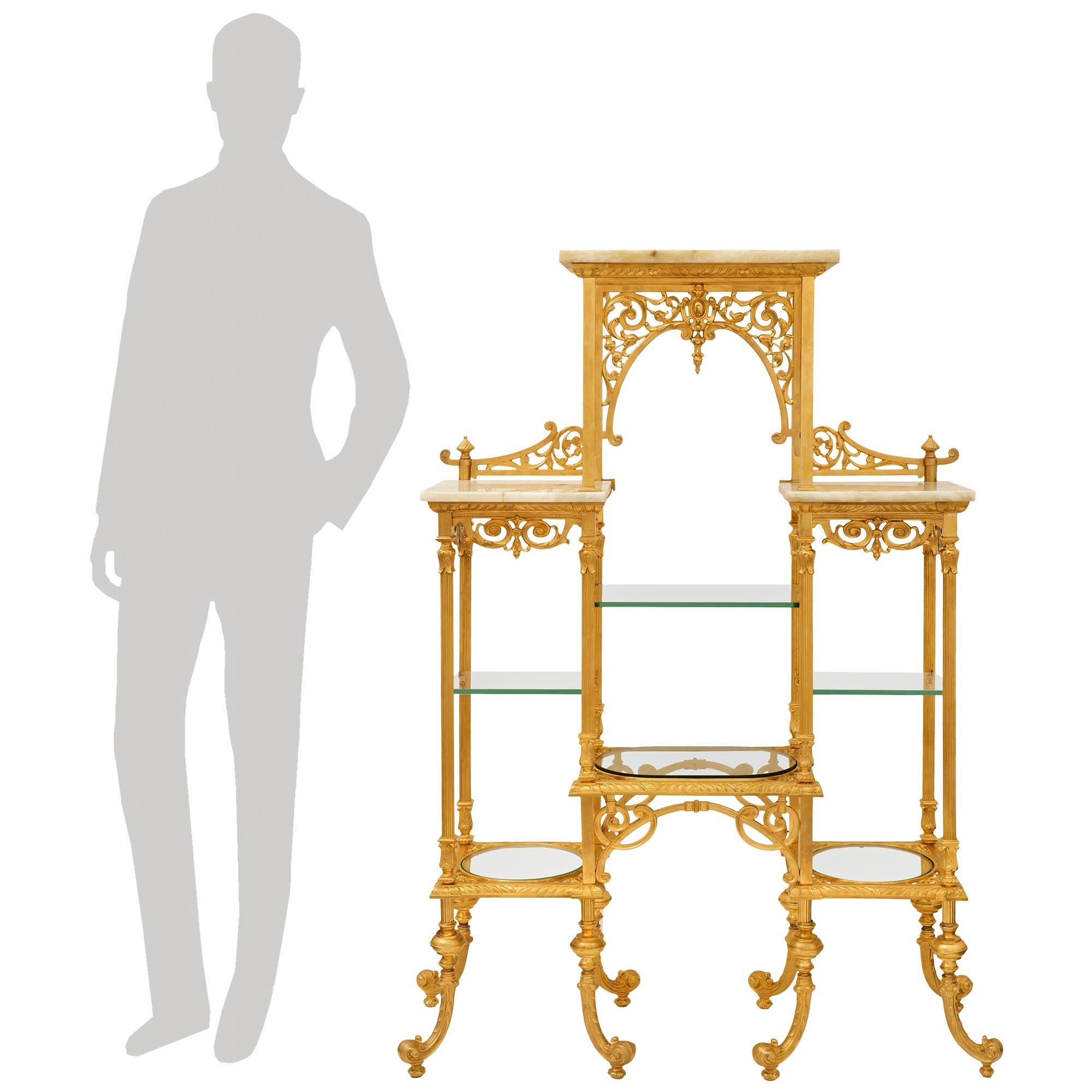 Un'elegante e decoratissima etagere/scaffale francese di fine secolo Luigi XVI in ormolu, onice e vetro. Questa splendida étagère è sollevata su otto gambe a volute foliate decorate con foglie d'acanto che conducono al livello inferiore di ripiani