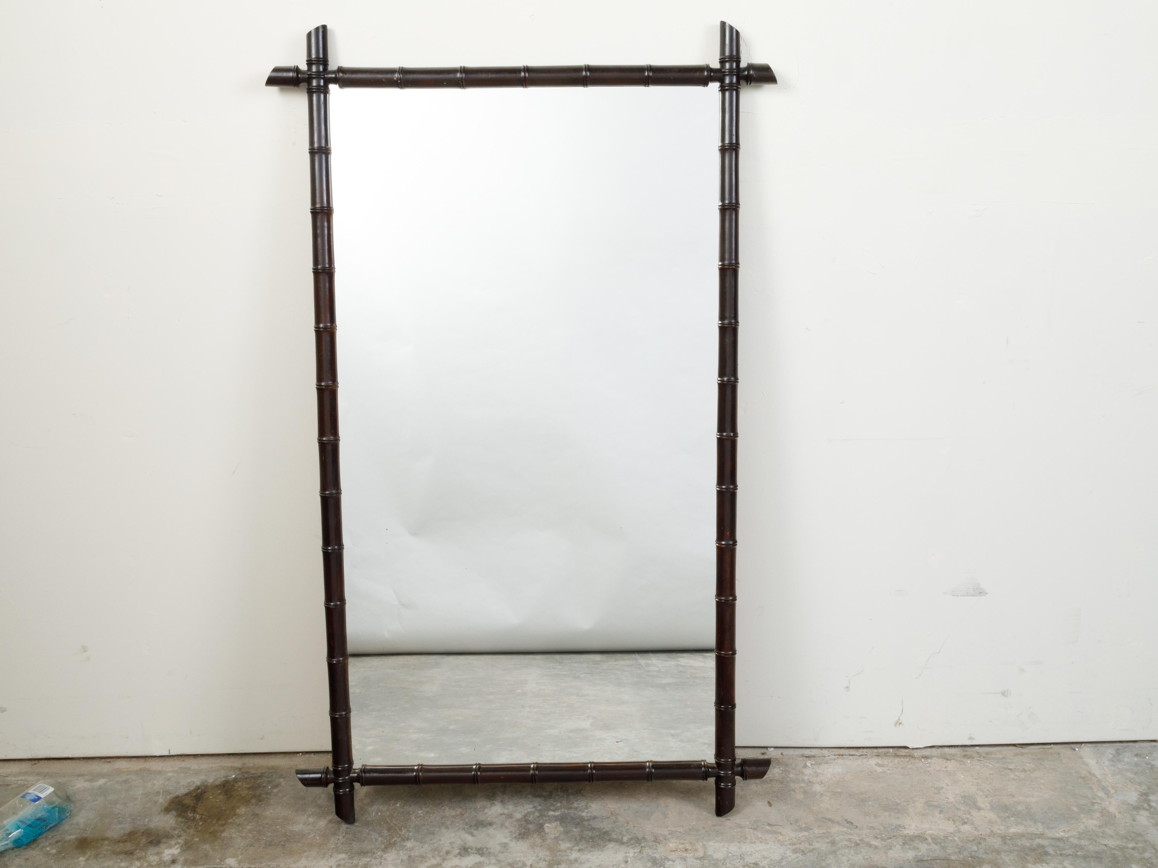 A French rectangular faux-bamboo mirror from the early 20th century, with black patina. Created in France during the Turn of the Century, this rustic mirror features a rectangular silhouette made of a thin black bamboo frame showcasing intersecting
