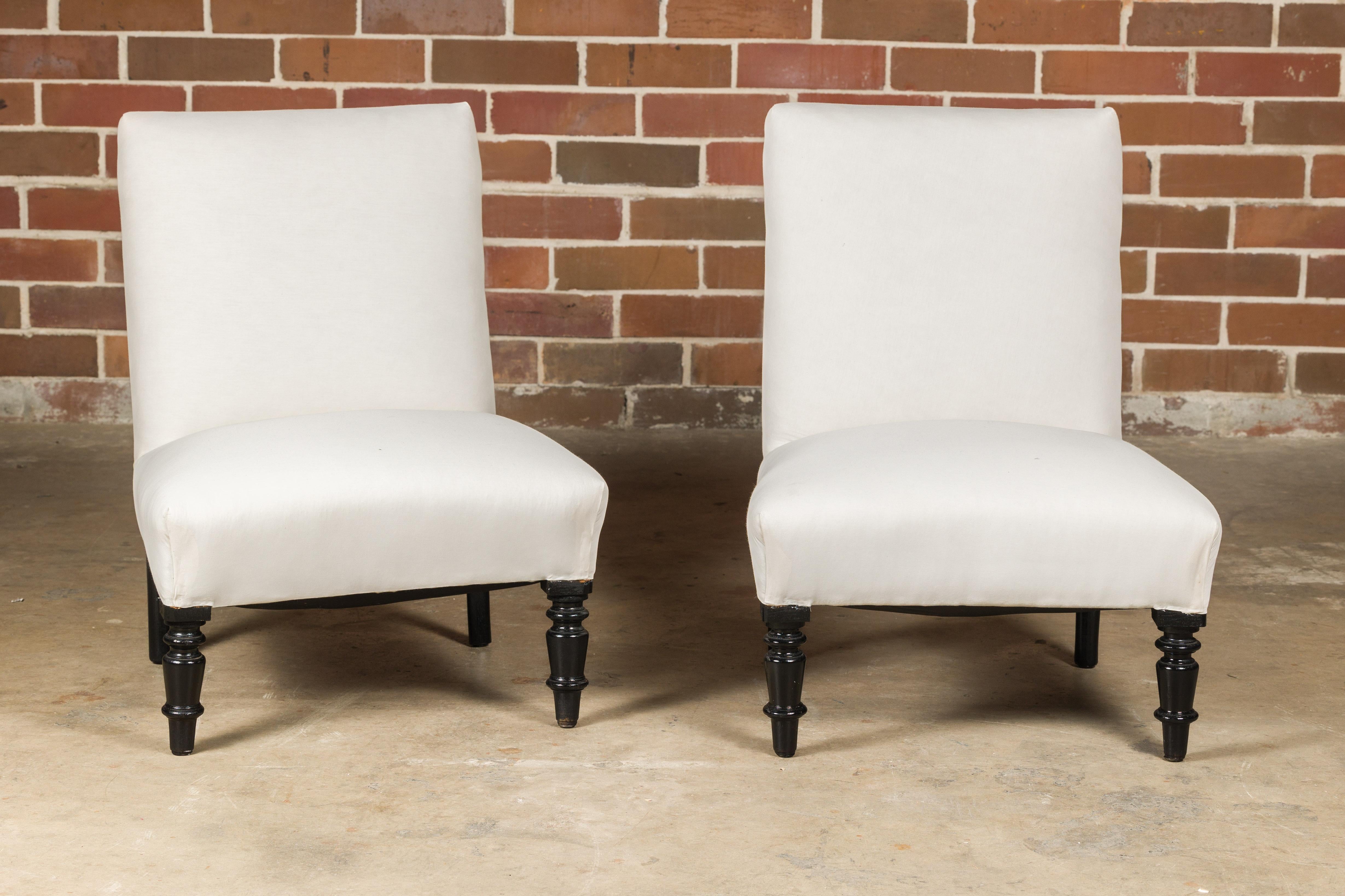 A pair of French slipper chairs from circa 1900 with ebonized turned legs and upholstered seats. Delve into the refined elegance of these French slipper chairs from circa 1900, pieces that exude the grace and sophistication of their time. With their