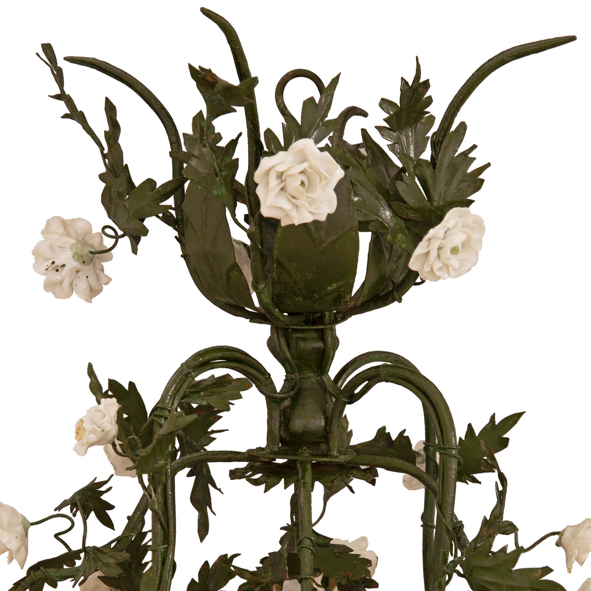 A beautiful and very charming French turn of the century tole and Blanc de Chine porcelain chandelier. The four arm nine light chandelier displays a most decorative scrolled cage wrapped with striking wonderfully executed vines with luxuriant tole