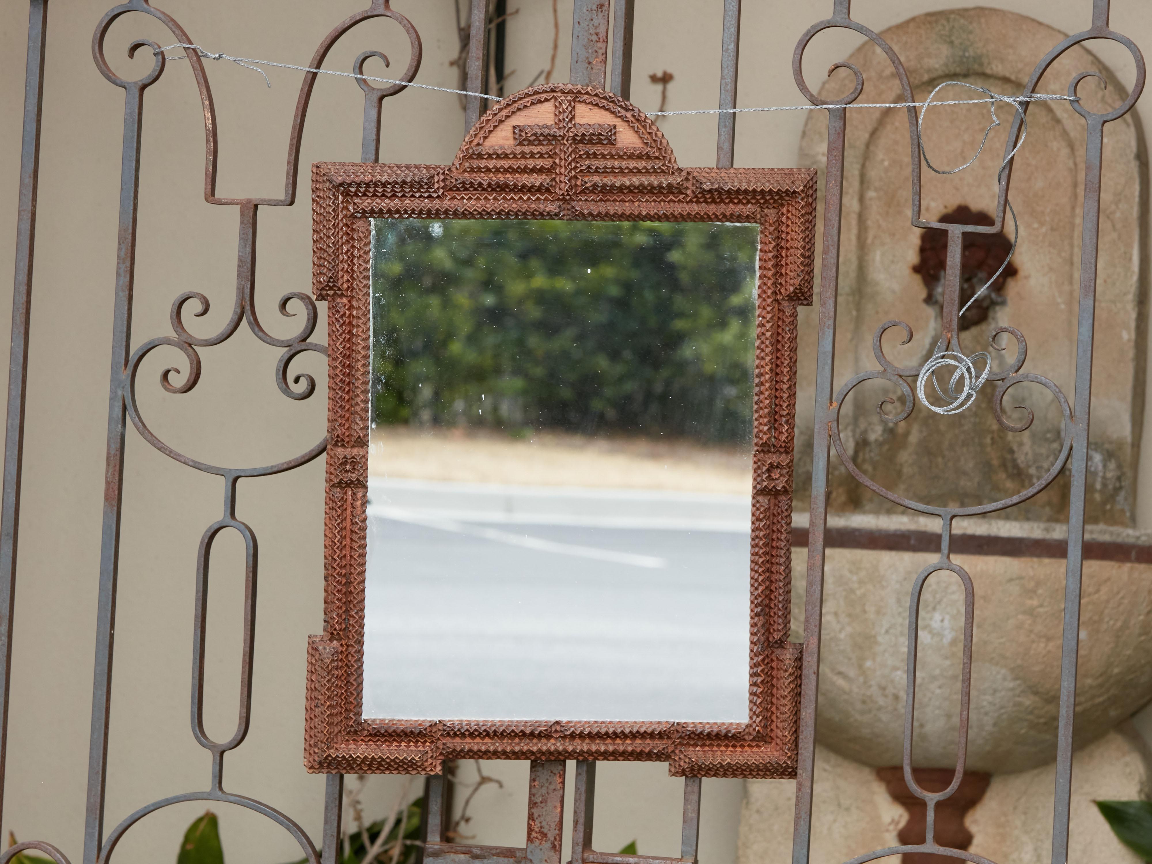 A French Turn of the century Tramp Art hand-carved mirror from the early 20th century, with arching crest, cross motif, protruding corners and brown patina. Created in France during the Turn of the Century which saw the transition between the 19th