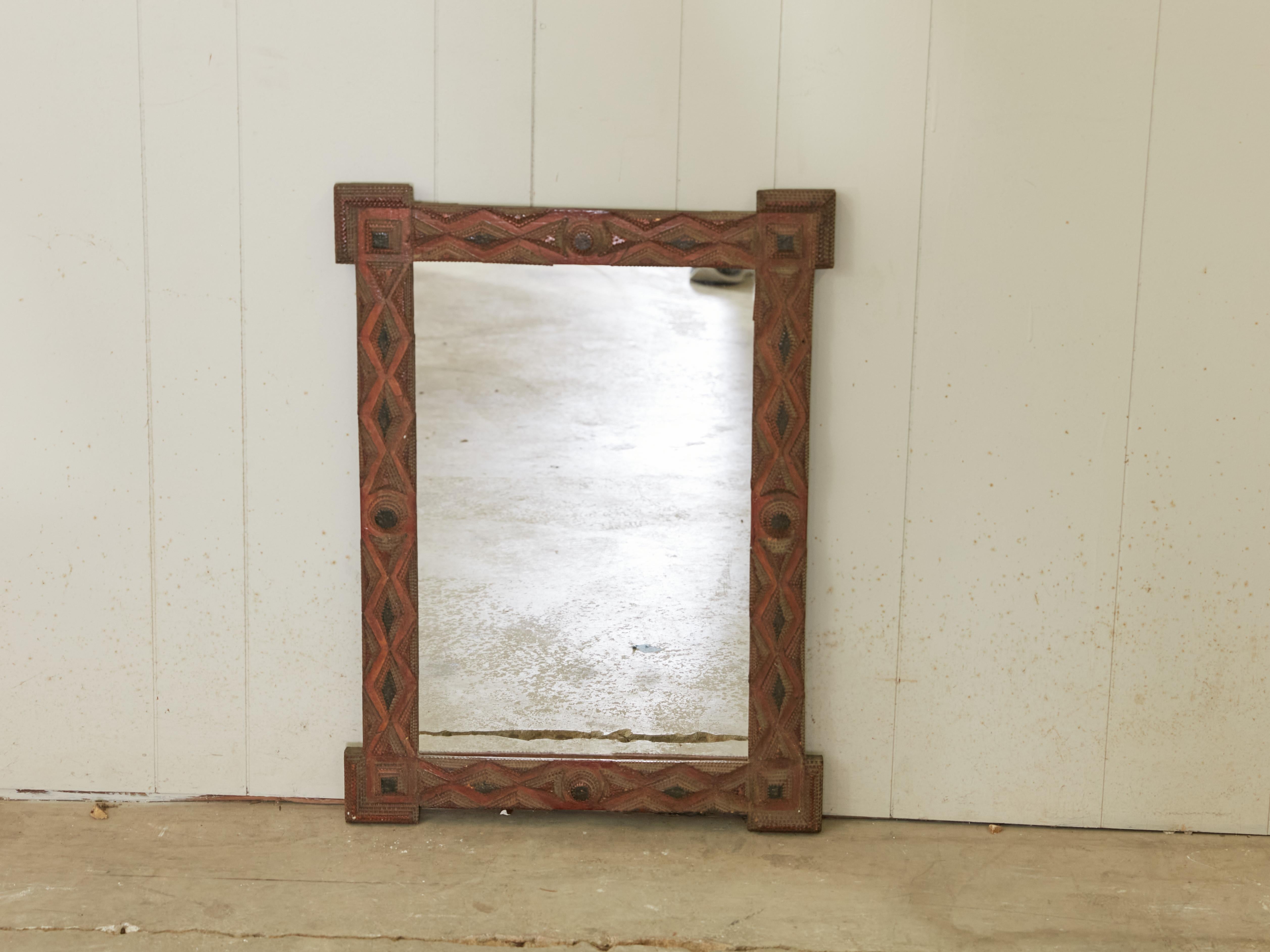 A French Turn of the century Tramp Art hand-carved mirror from the early 20th century, with protruding corners, raised geometric motifs and black and brown patina. Created in France during the Turn of the Century which saw the transition between the