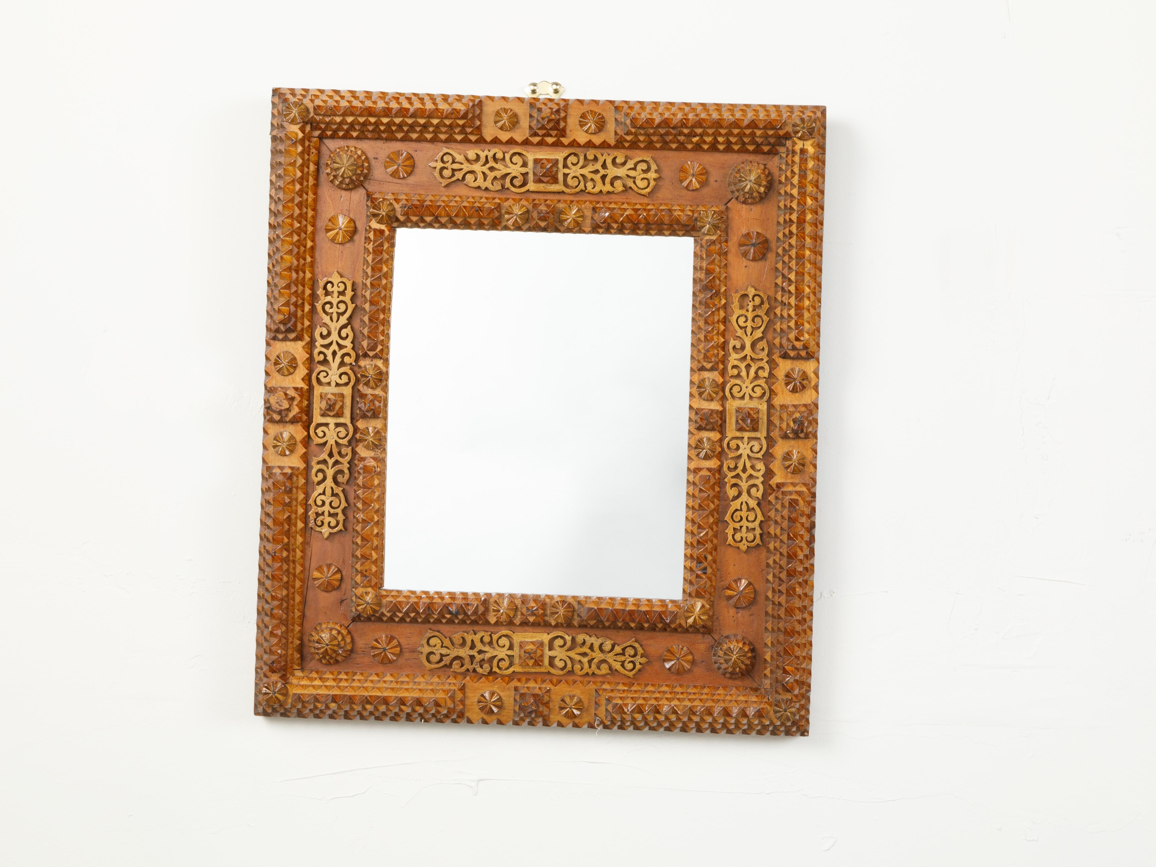 A French Tramp Art mirror from the early 20th century, with raised rosettes and ornate brass accents. Created in France at the Turn of the Century, this wall mirror was hand carved in the manner typical of the Tramp Art style. Presenting a linear