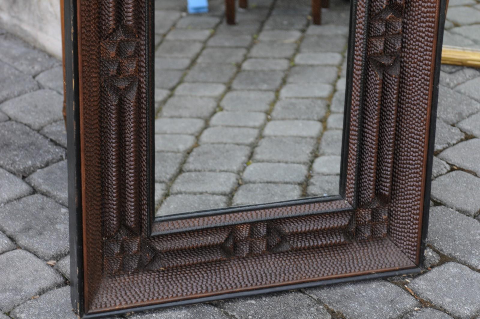 A French Tramp Art wall mirror from the early 20th century, with brown patina and textured motifs. Born in France during the turn of the century, this wall mirror features a rectangular beveled frame, adorned with the typical Tramp Art touch made of