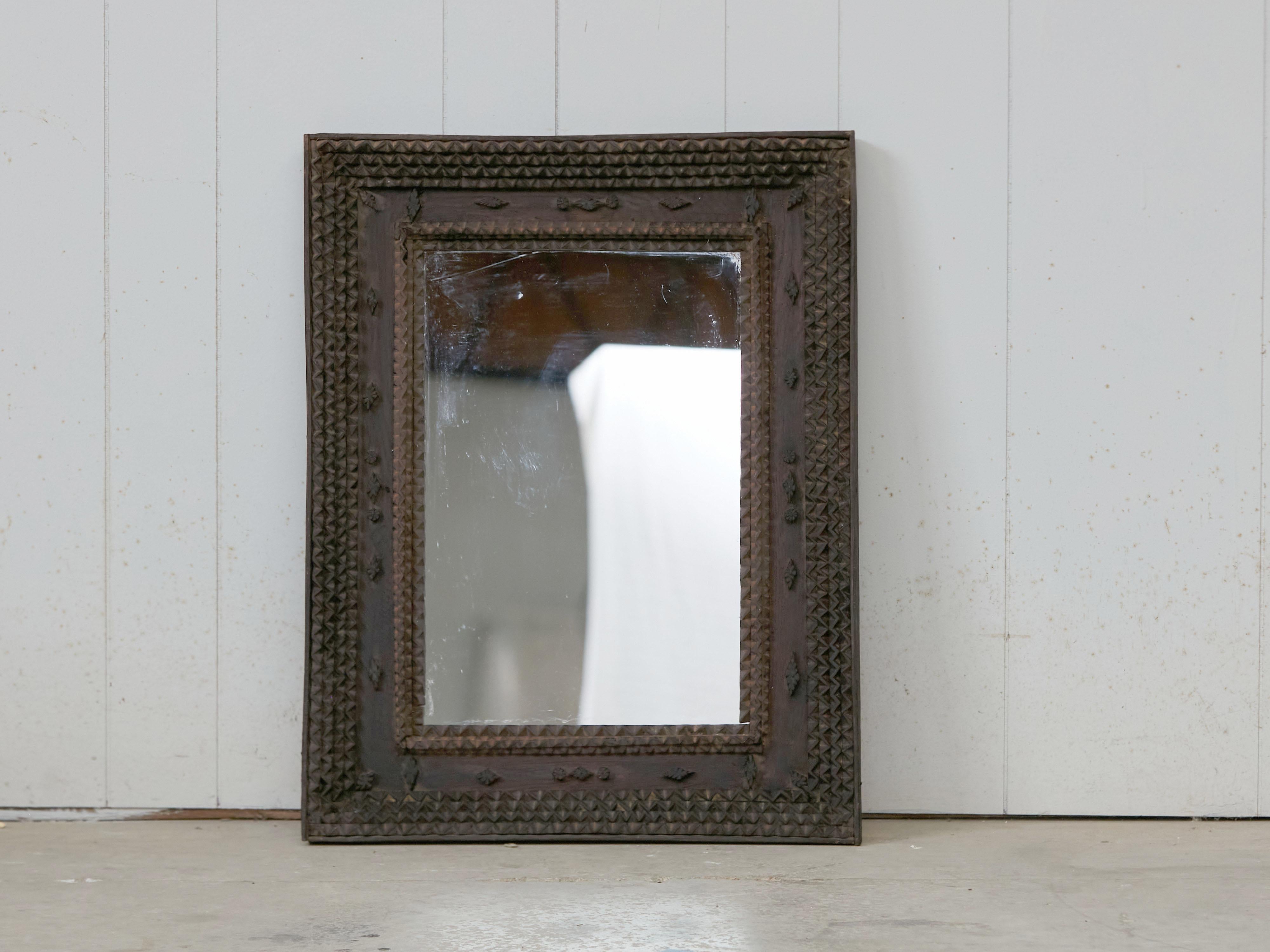 A French Tramp Art wall mirror from the early 20th century, with brown patina, and carved rosettes. Created in France during the turn of the century, this wall mirror features a rectangular frame, adorned with the typical Tramp Art touch made of an