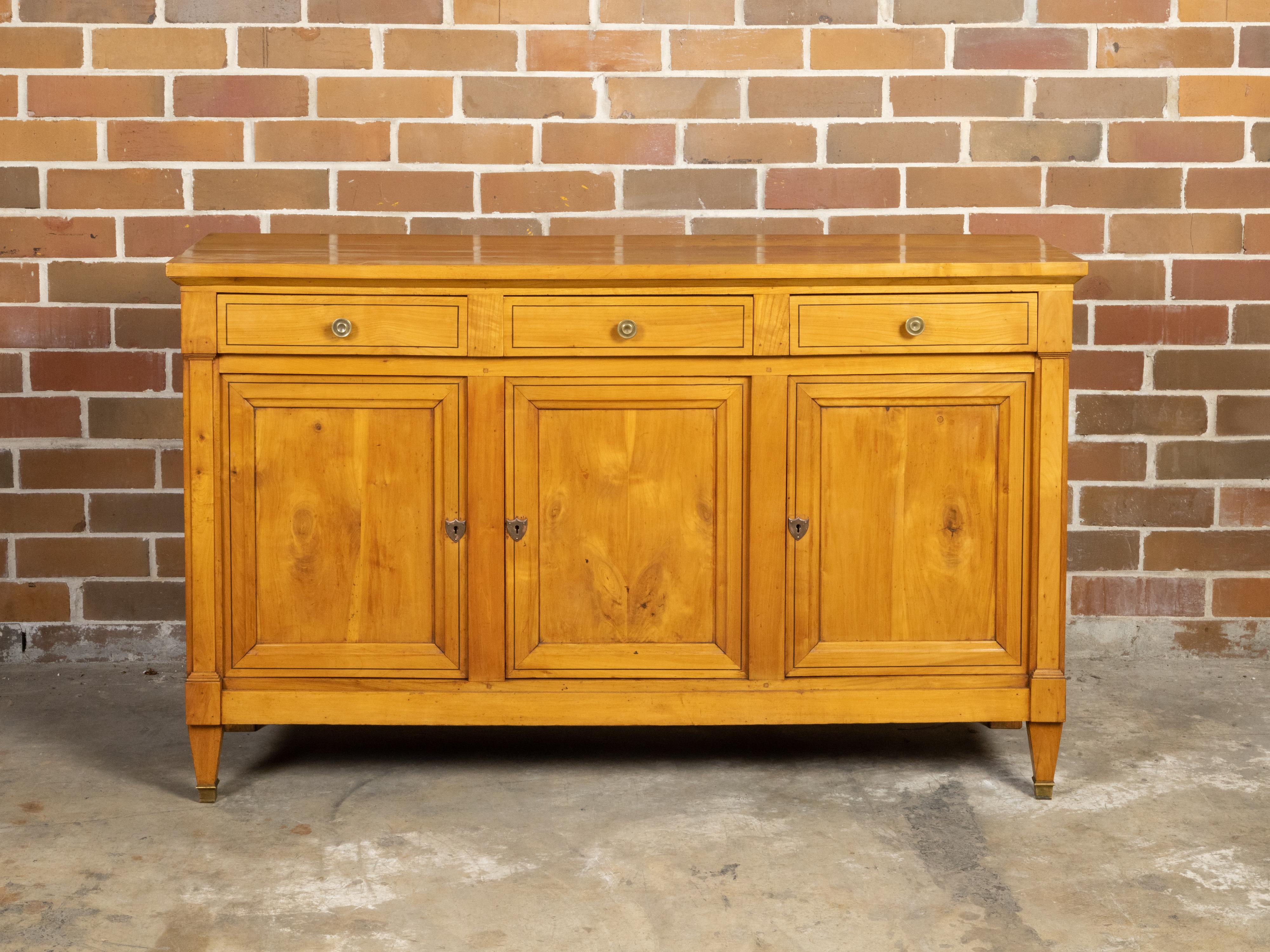 A French Turn of the Century walnut buffet from the early 20th century, with three drawers over three doors, brass pulls and feet, pilaster motifs, banding and tapered legs. Created in France during the Turn of the Century which saw the transition