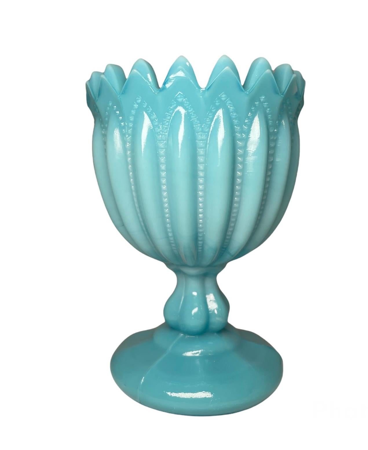This is a Portieux Vallerysthal opaline milk glass goblet vase. The zigzag rim bowl is adorned with ribbed drop shaped lines and the stem is lobulated. Below the round base, there is a starburst decoration.