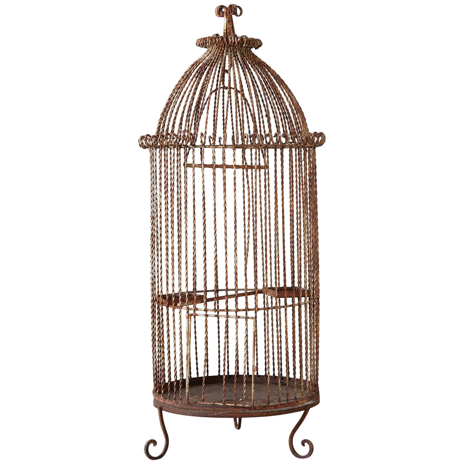 Rustic French standing bird cage made of wrought iron and thick twisted wire. The round form has a domed top with scrolls. There is a large swinging perch inside and large door. The cage is supported three scrolled legs and the piece has a lovely