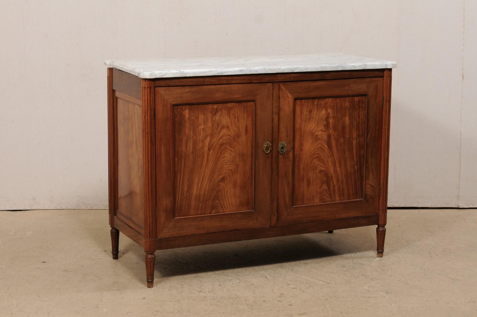 A French two-door chest, with it's original marble top, from the early 19th century. This antique chest from France features a rectangular-shaped marble top with pronounced and rounded corners, with rests atop a neoclassical style case with fluted