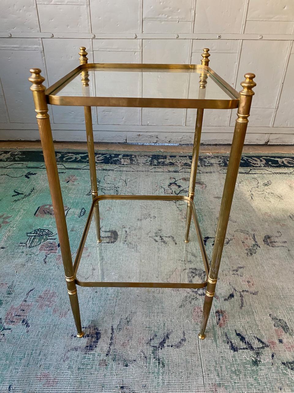 An exceptional neoclassical style brass and glass two-tiered side table with rounded edges. This beautiful neoclassical style side table exudes an air of elegance and sophistication. Crafted from brass and glass, this two-tiered table is a true work