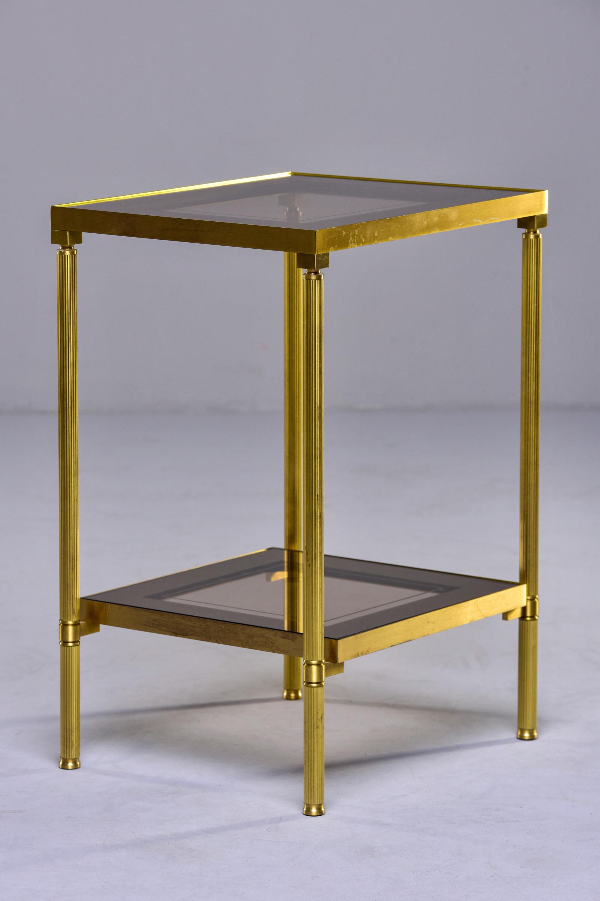 Circa 1940s French side table with brass frame and smoked glass table top and lower shelf with gold mirrored border. Unknown maker.