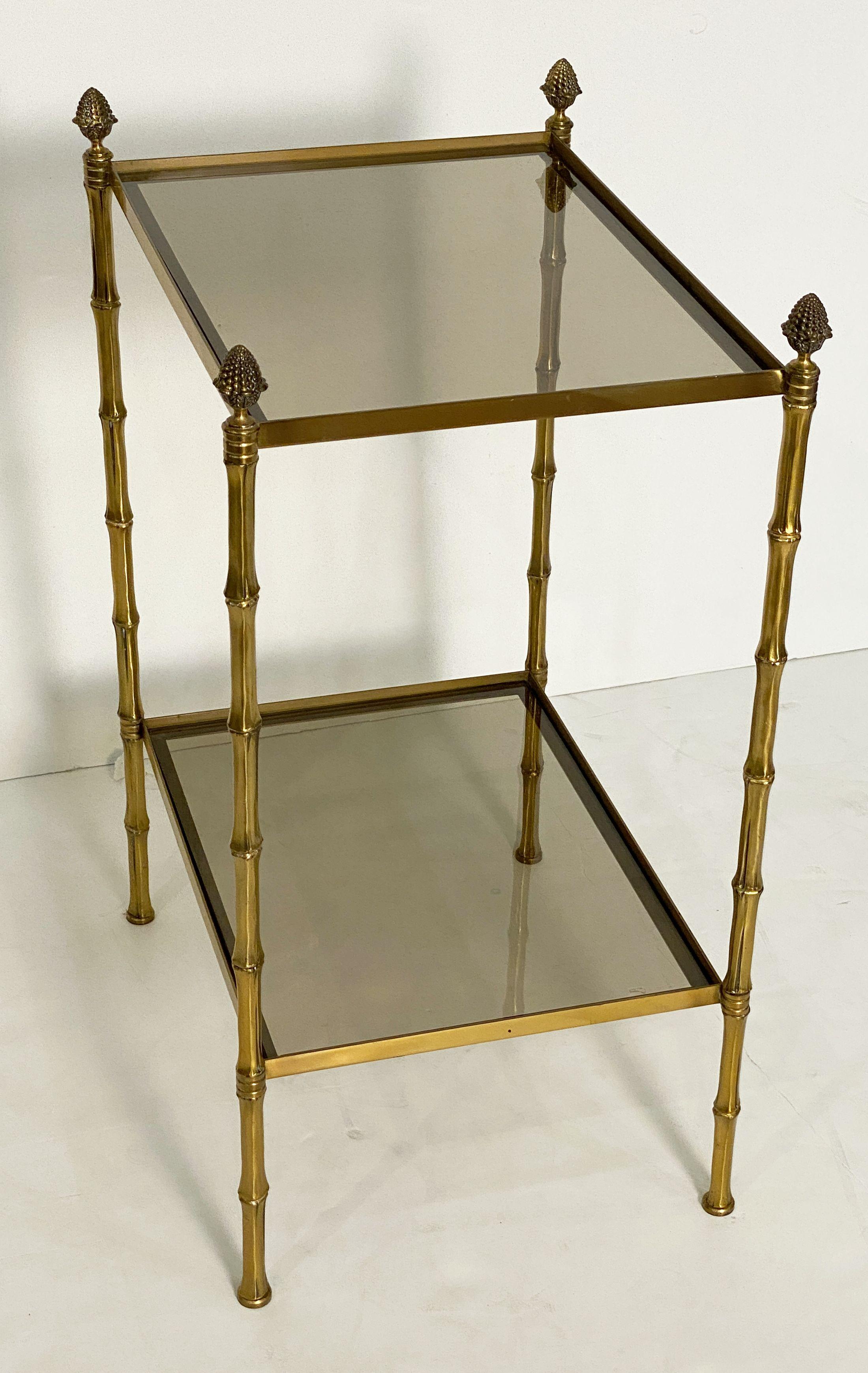 A fine French Mid-Century Modern rectangular end or side table, featuring two tiers of smoked glass and a stretcher frame of brass with finials and tapering legs with a faux bamboo design.