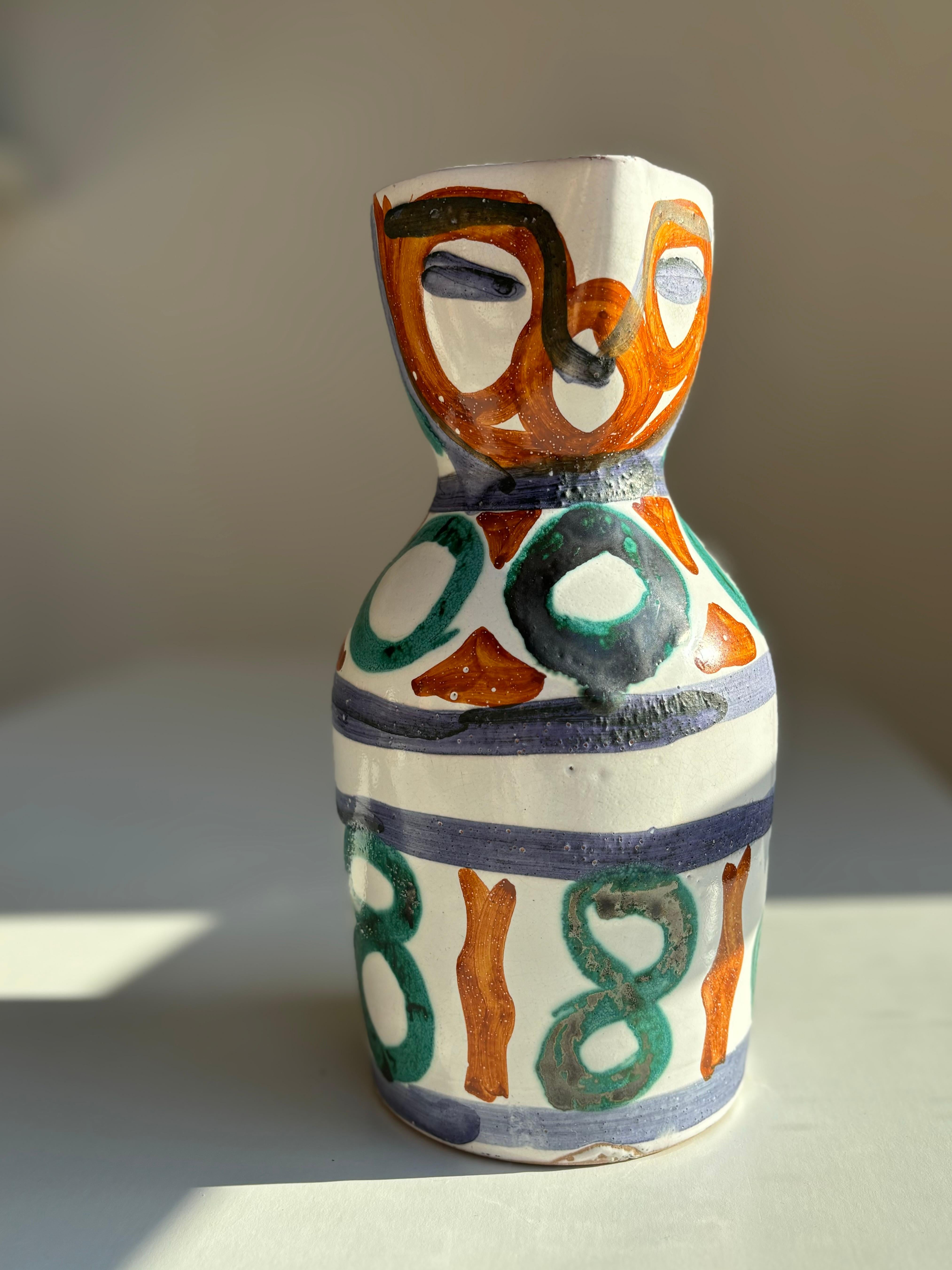 Vaso a brocca in ceramica francese vintage di Vallauris. Decoro astratto simile a un volto con pennellate color ambra, verde scuro e blu notte su una base bianca e nitida. Firmato sotto la base.
Bellissime condizioni vintage.
Francia, anni '50.