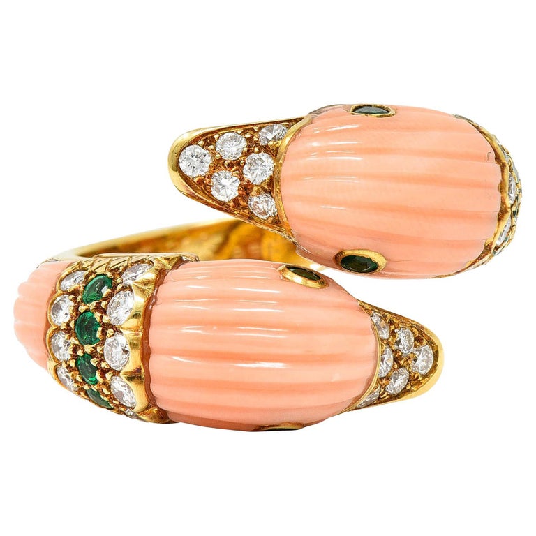 Bypass style ring features terminals formed as ducks

With fluted pink coral - pastel in color and very well matched with no mottling

Accented by bright green emerald eyes and neck band - weighing in total approximately 0.36 carat

With round