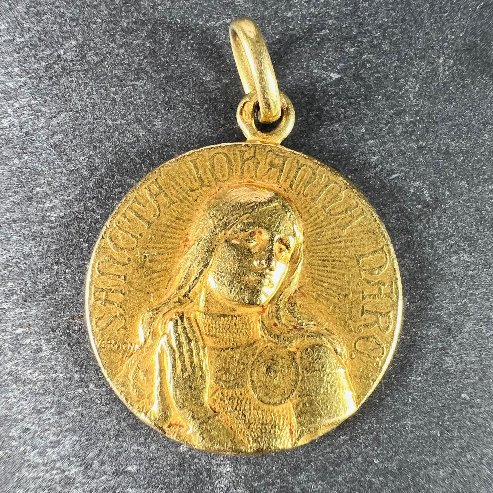 A French 18 karat (18K) yellow gold charm pendant designed as a round medal with a relief of Joan of Arc in armour to one side praying, the words 'Sancta Johanna D'Arc', to the reverse a shield bearing her coat of arms with lilies and ribbons.