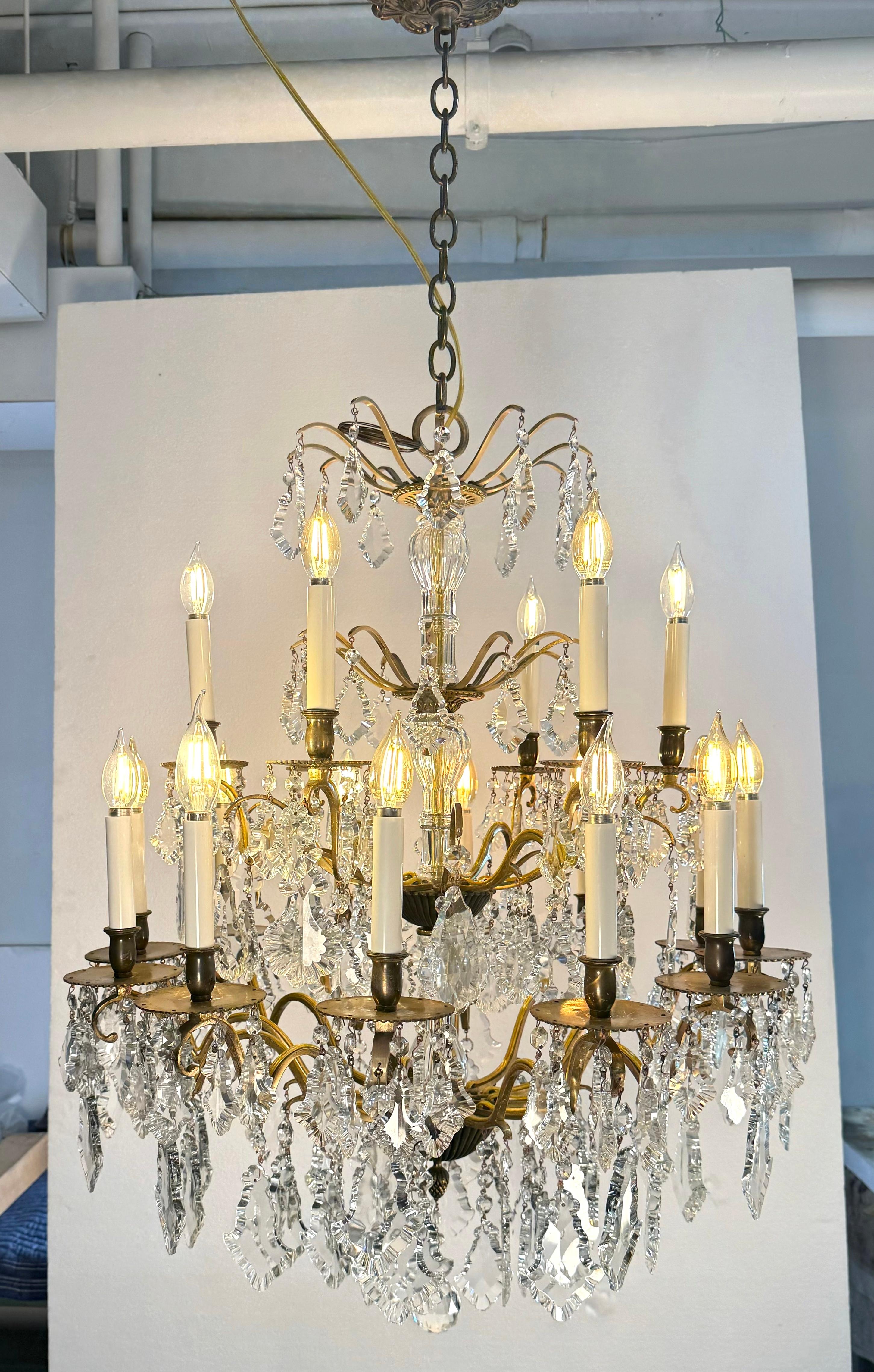 Lampadario a due piani in stile francese con struttura in ottone. Con cristalli francesi trasparenti a forma di pendolo di Versailles e un pendente di cristallo sfaccettato. Questa lampada richiede 18 lampadine E-12 a candelabro. Questa luce è stata