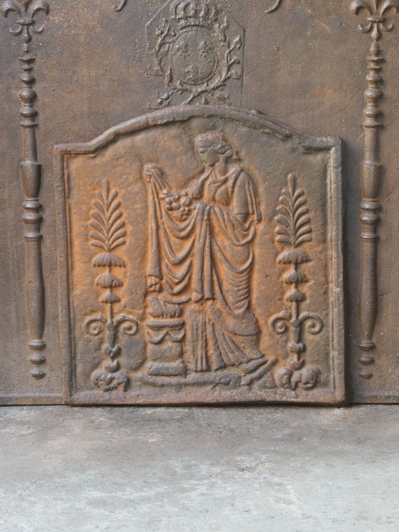 20th century French 'Vestal Virgin' fireback / backsplash with Victorian style features. Made of cast iron with a natural brown patina. Upon request, it can be made black / pewter. The fireback is in good condition and does not have cracks.