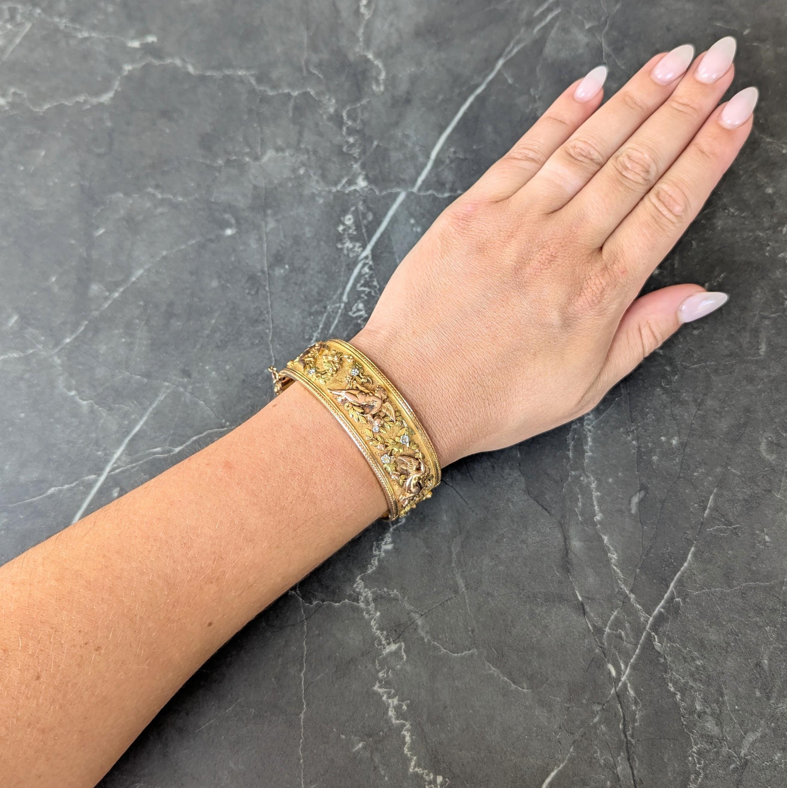 Diseñado como un brazalete ancho compuesto por paneles curvados de oro amarillo con textura en toda su superficie
Con un aplique de querubín de oro rosa pulido en varias posiciones, totalmente alrededor
Acentuado por enredaderas de follaje verde