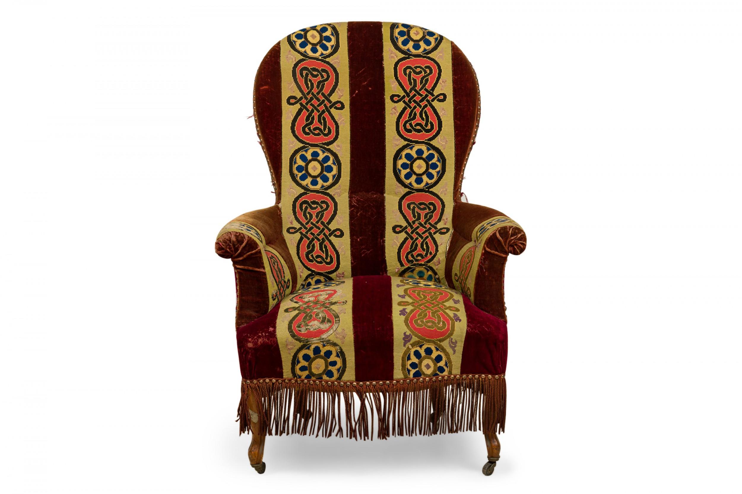 French Victorian balloon back armchair upholstered in a deep red velvet with broad vertical stripes featuring knit and floral designs in beige, pink, and blue, resting on four shaped mahogany legs ending in small brass casters, partially concealed