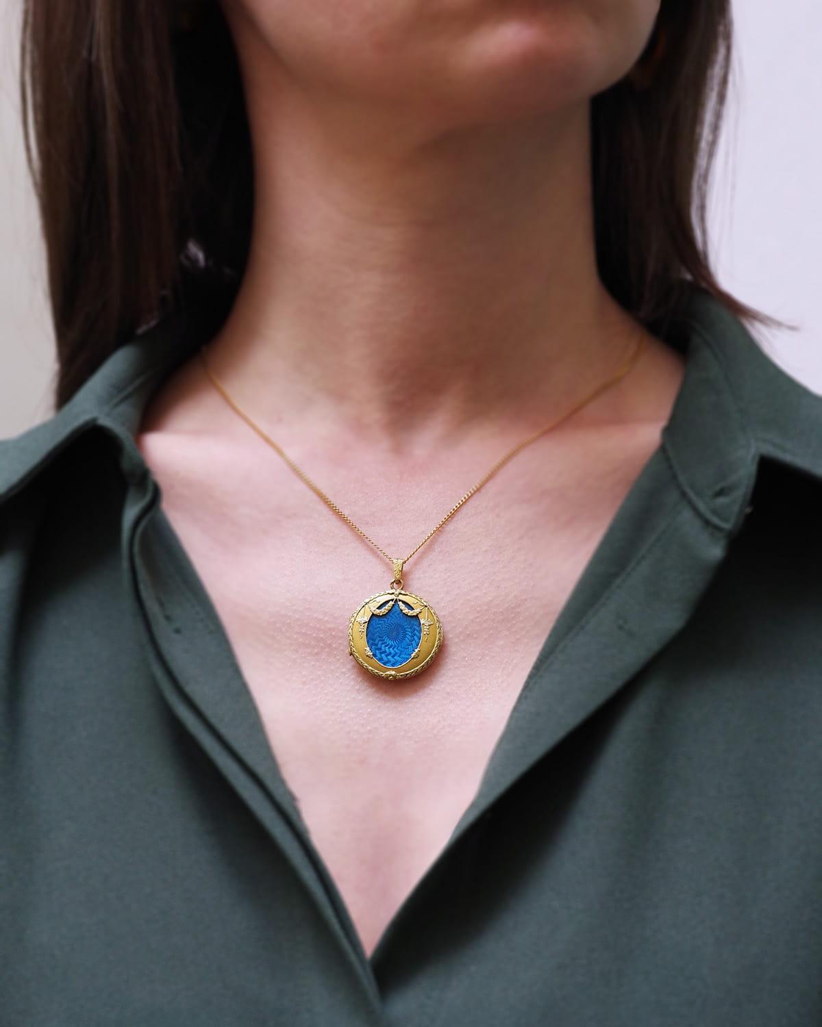 Ciondolo vittoriano a forma di medaglione in oro 18 carati. Pendente a medaglione del periodo di Napoleone III decorato con smalto blu guilloché in un motivo di ghirlande di fiori e un fregio di alloro. Il medaglione si apre per contenere un oggetto