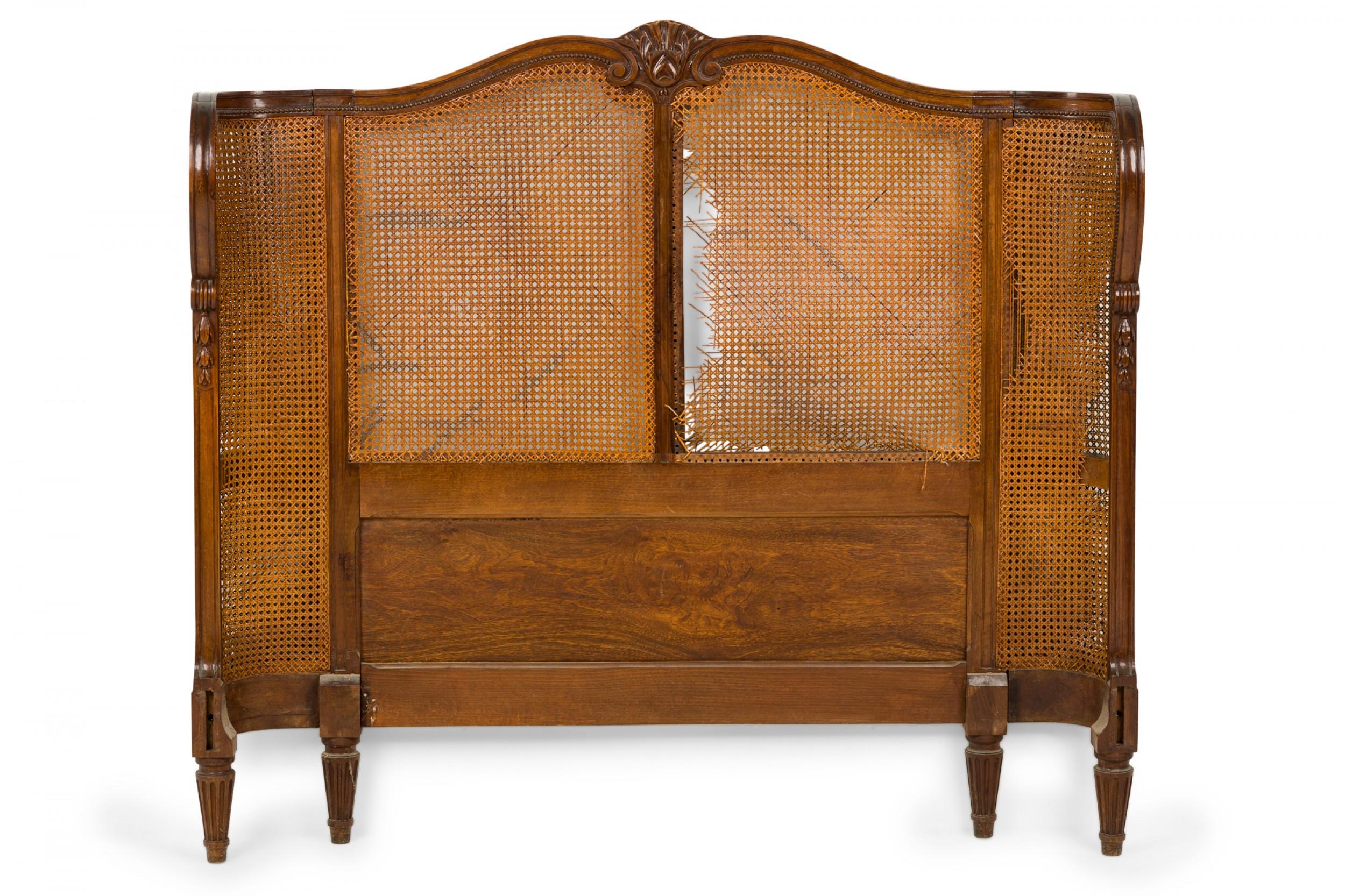 French Victorian queen-size bed frame comprised of a headboard with carved wooden frame featuring shell and foliate designs, a footboard with a carved wooden central bow and fruit oval medallion, all with caned panels, resting on tapered and fluted