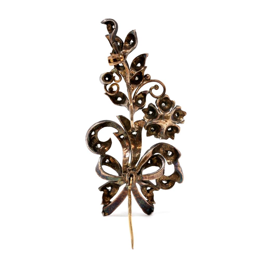 The original early Victorian brooch originated in France circa 1870-80. It is made with silver applied on gold, like many pieces from that period. The pin represents a floral motif set with rose-cut diamonds and pearls. It measures 2.13 inches long