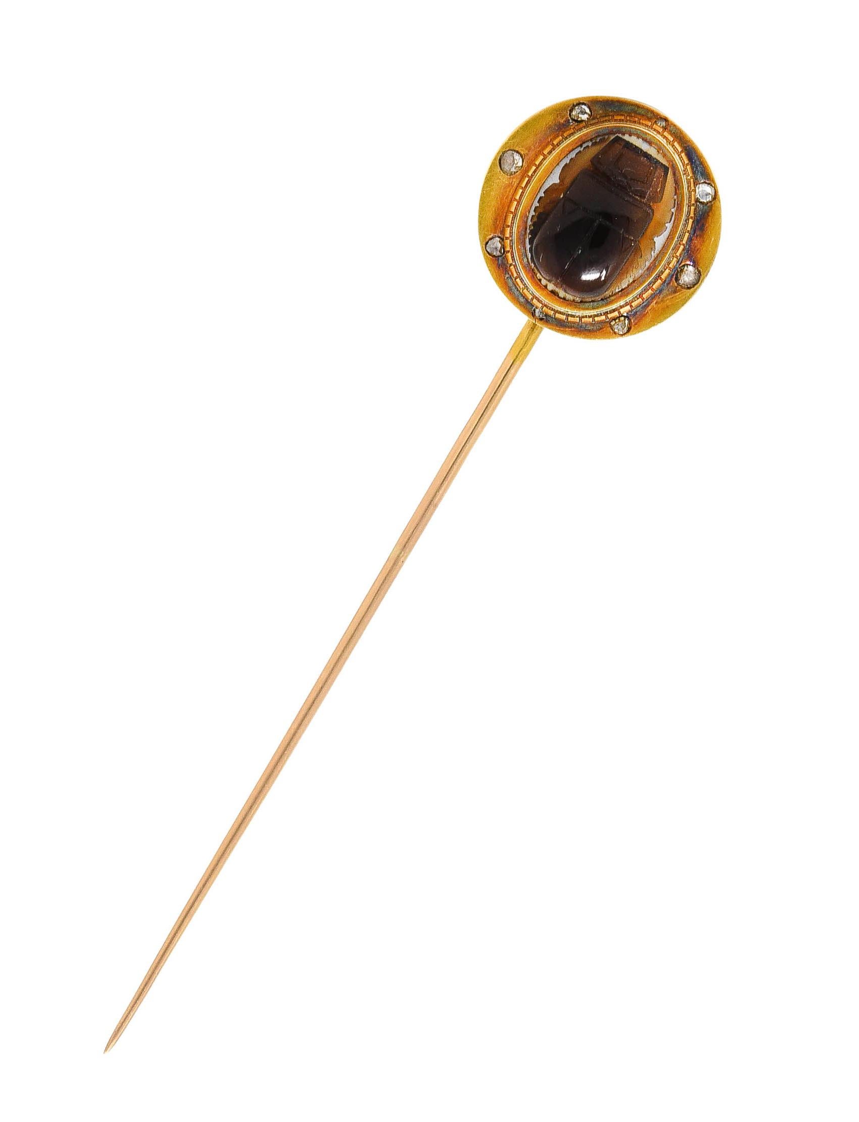 Stickpin centers agate carved to depict a scarab - translucent orangey brown with medium dark saturation

Measuring 9.5 x 12.0 mm - backed by opaque white agate and bezel set

With grooved gold surround accented by flush set rose cut