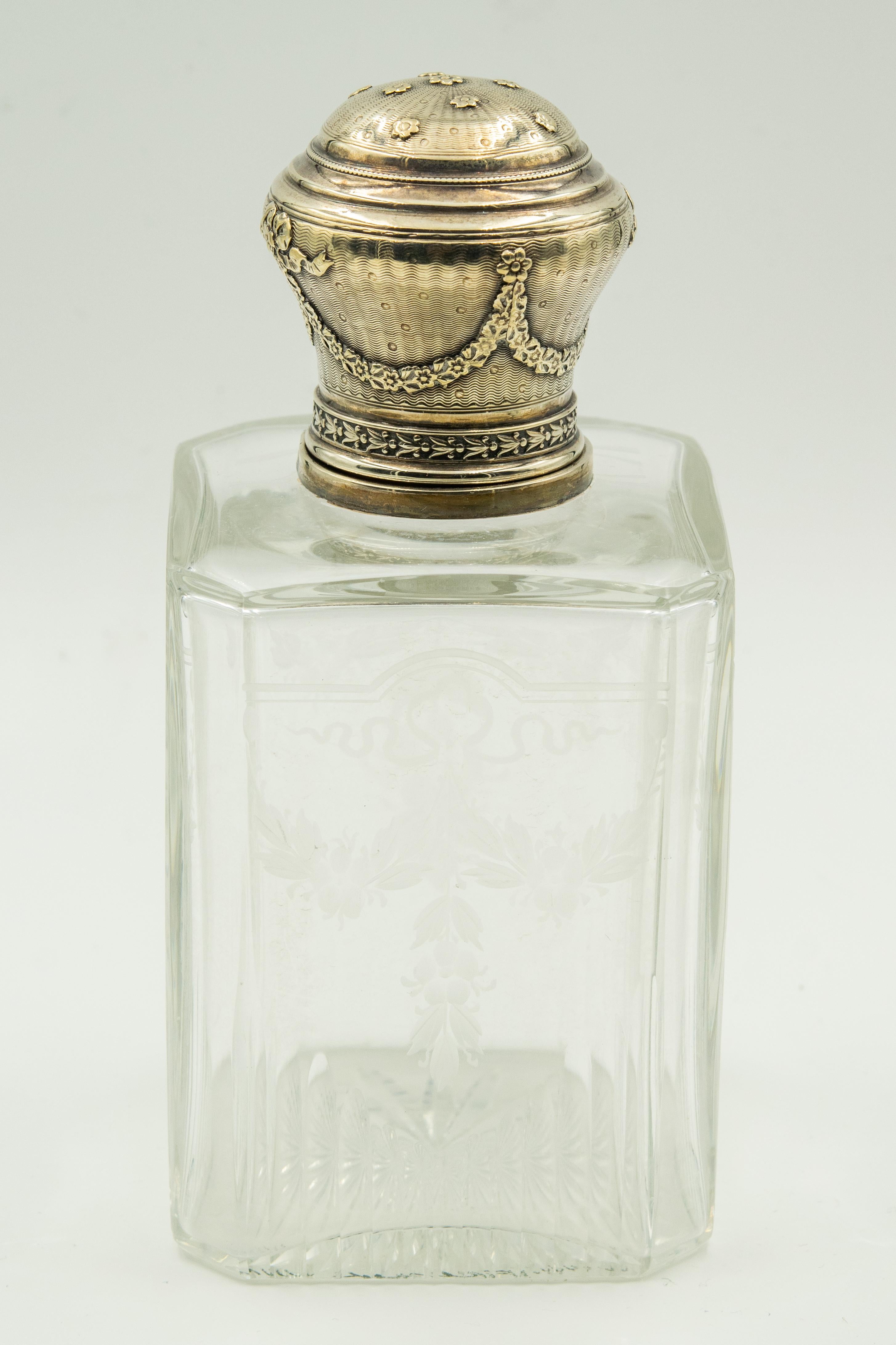 Beautiful French antique crystal bottle etched with ribbons and floral sprays and fluted bottom. The top of the bottle has a sterling silver rim which is topped with an ornate sterling bottle top. The top has an engined turned background accented