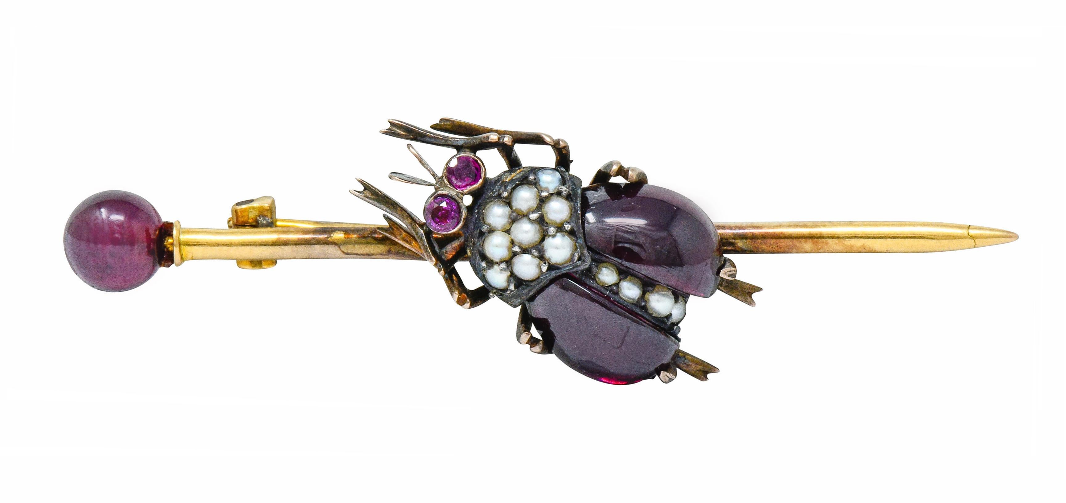 Featuring a stylized beetle with garnet cabochon wings; deeply reddish-purple

Accented by 1.5 mm round natural freshwater pearls, cream in body color with very good luster

Heavily oxidized with spindly legs and round cut ruby eyes, well-matched to