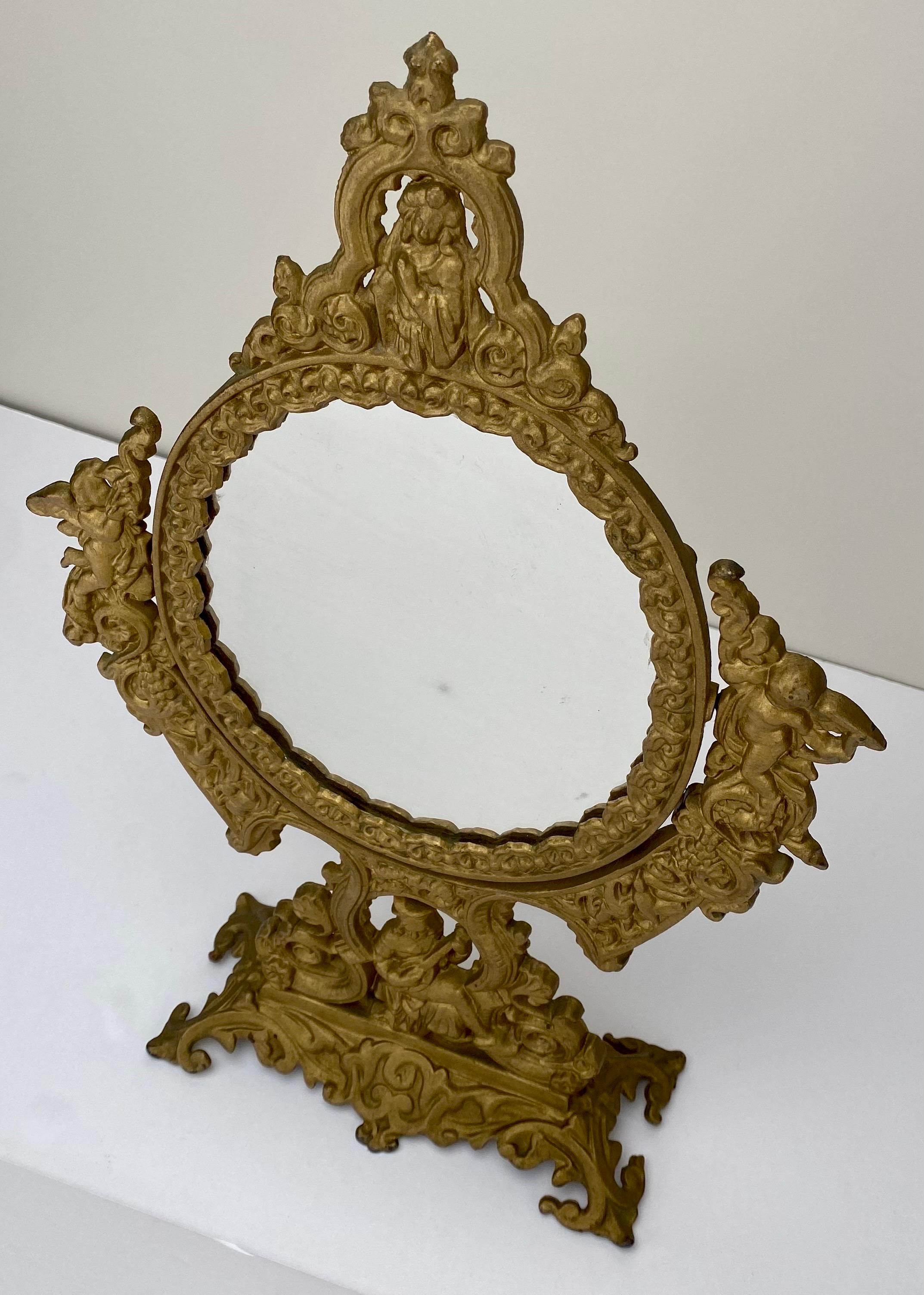 An exquisite antique French Victorian gilded bronze vanity mirror exuding a timeless charm from the late 19th Century. A multifaceted marvel, it features a swiveling oval mirror, gracefully adorned on each side by cherubic embellishments, while at