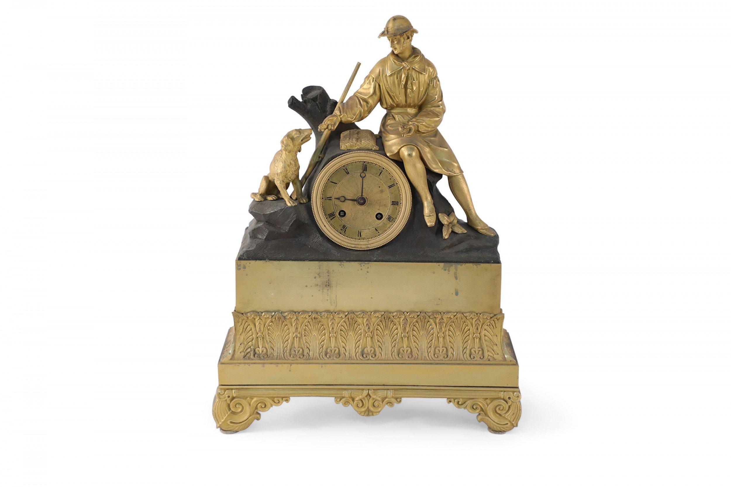 French Victorian (mid-19th Century) gilt bronze mantel clock featuring a hunter feeding his dog as they sit atop a bronze log which houses a gilt bronze clock face with hand painted numbers above an ornate gilt bronze rectangular footed base with a