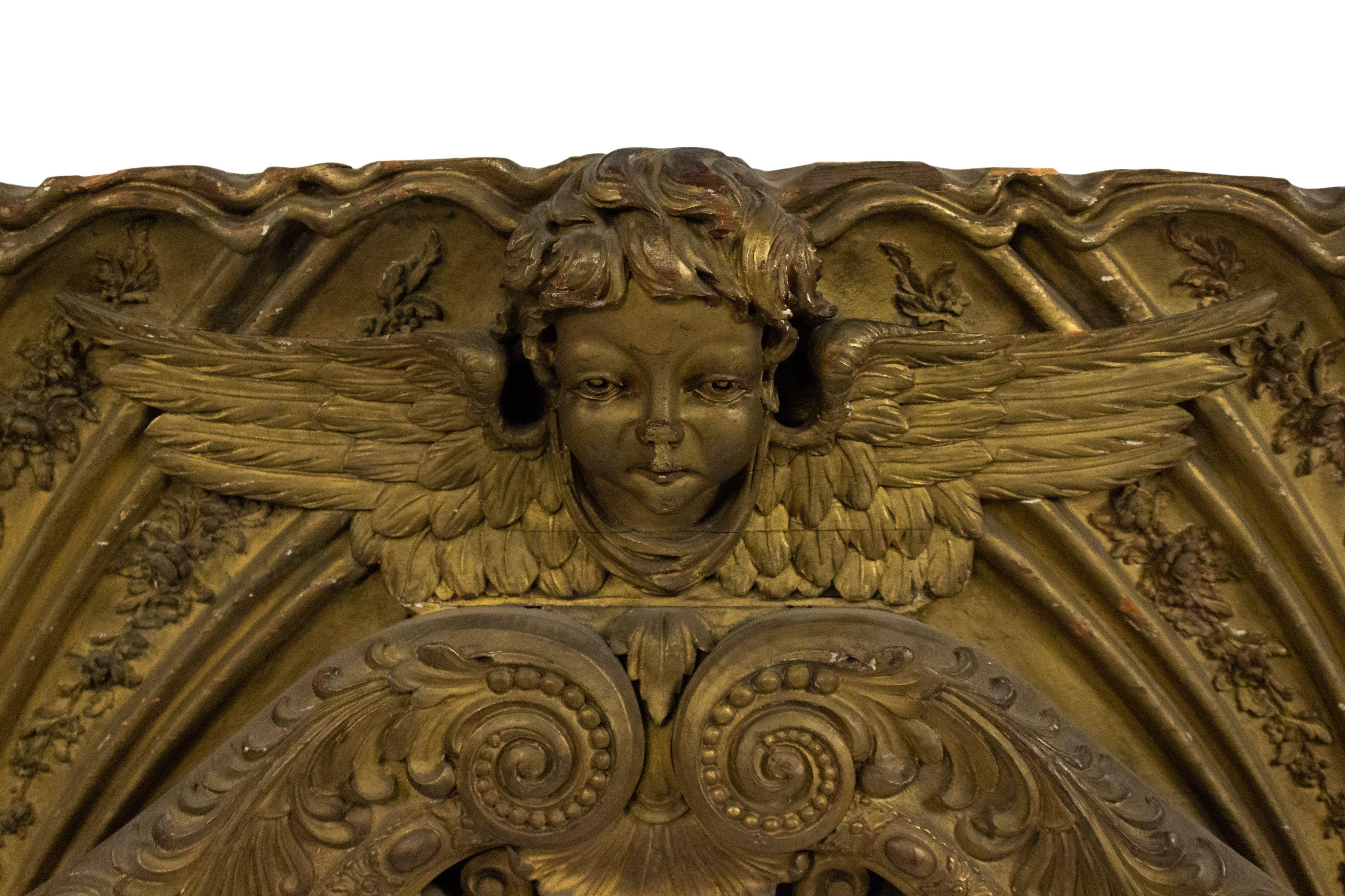 French Victorian large gilt arch shaped horizontal wall plaque with 3 carved winged cupid heads and scroll filigree design.
  