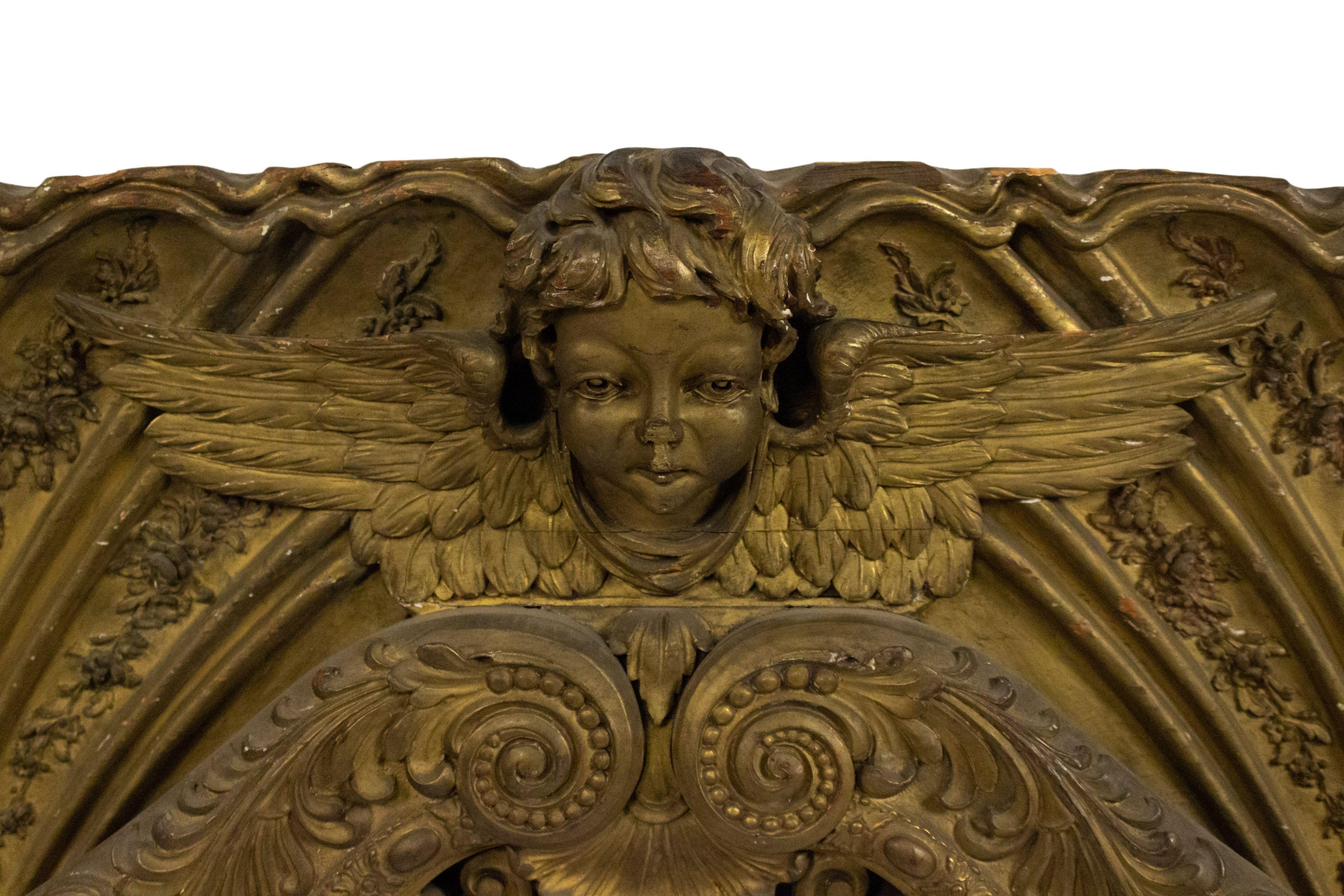 Gran placa de pared horizontal victoriana francesa en forma de arco dorado con 3 cabezas de cupido aladas talladas y diseño de filigrana en volutas.
  