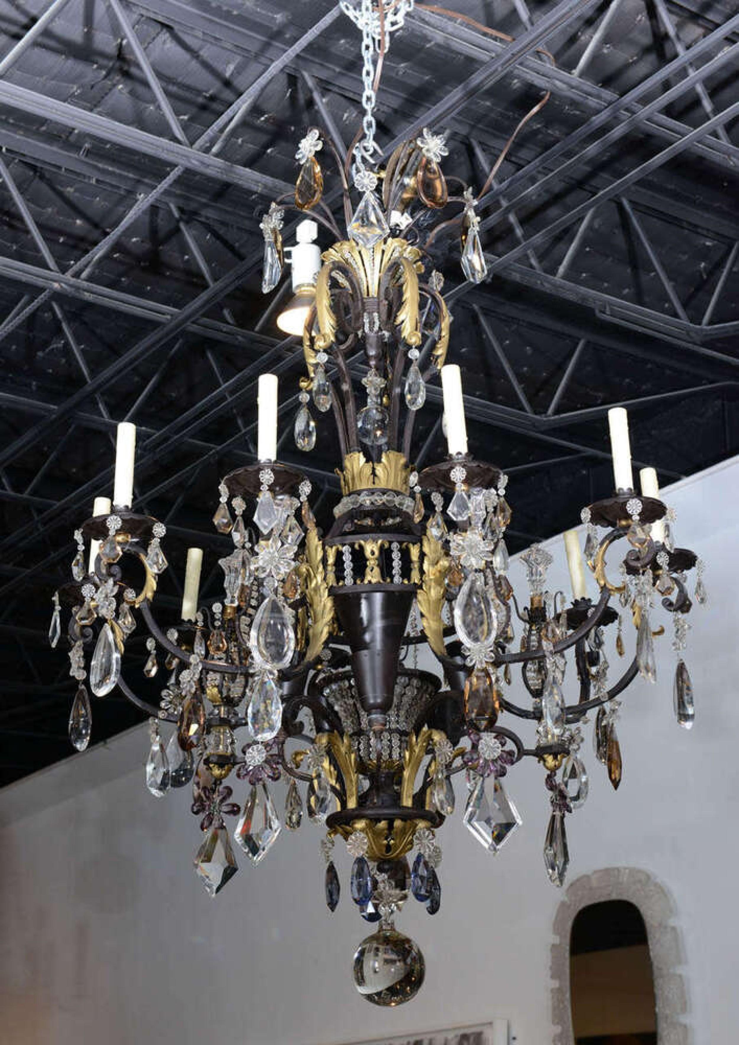 Lampadario francese degli anni '40 a 12 bracci in ferro e finiture dorate con gocce di cristallo ovali e a forma di diamante che pendono da bobeches in ferro e da vari prismi di cristallo di rocca e con un grande terminale a sfera in basso