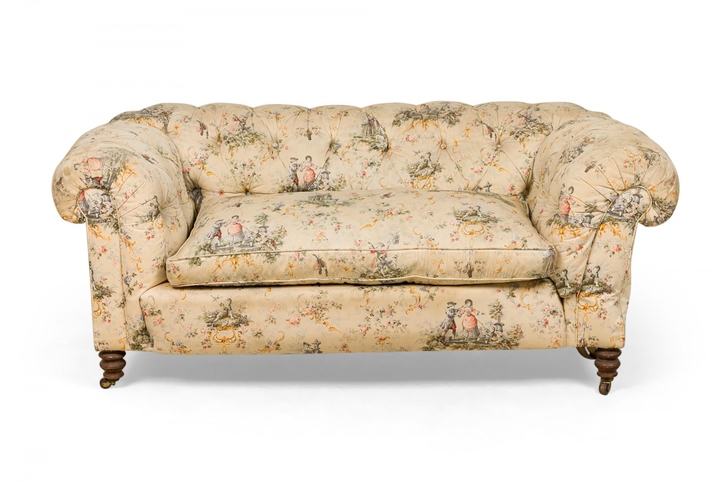 French Victorian-style loveseat upholstered in a toile print fabric with a beige background with multi-colored pastoral scenes throughout, accented with button tufting, resting on two turned mahogany front legs and two square carved back legs, all