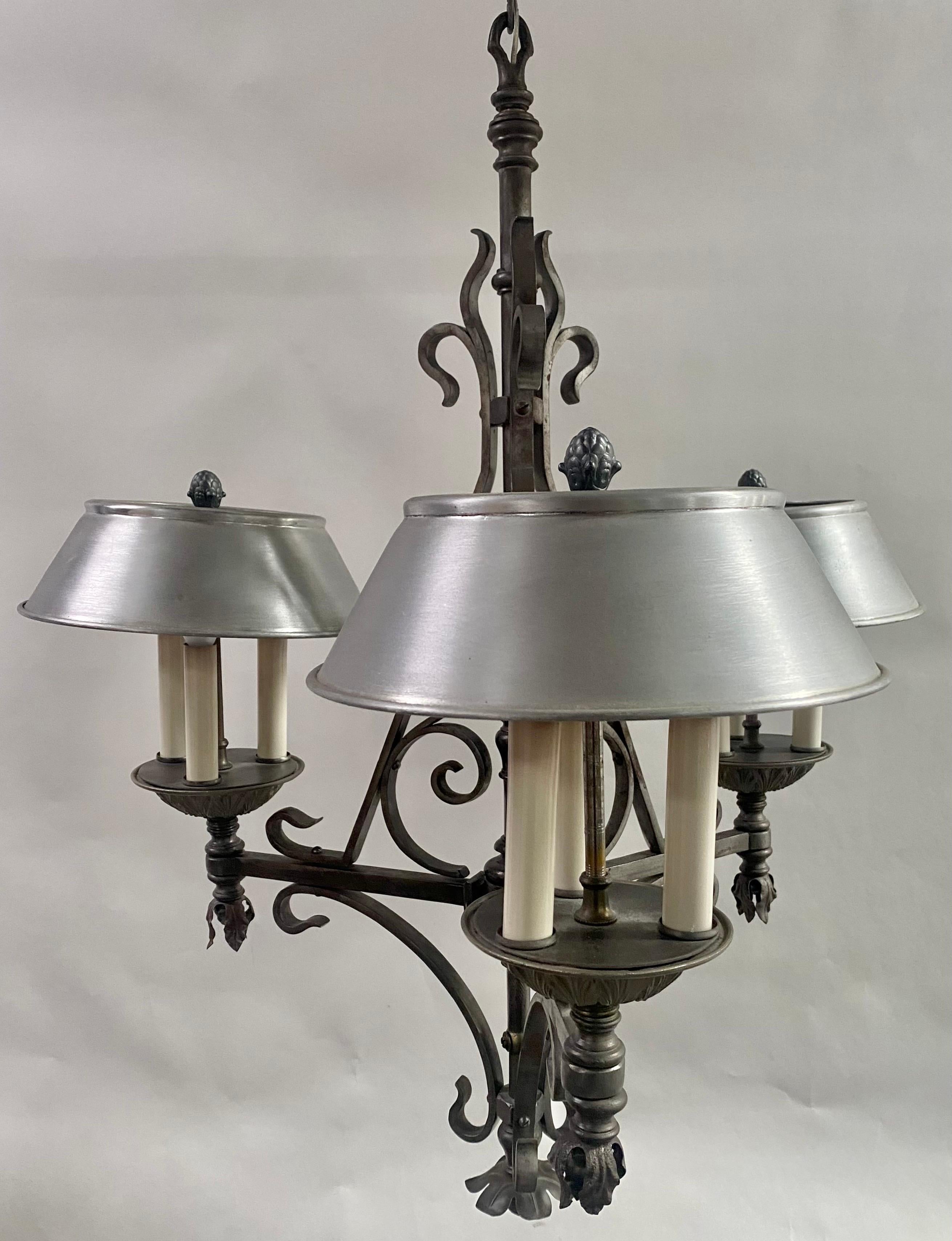 A 1930's French Victorian style wrought iron chandelier. This resplendent fixture boasts an intricate design characterized by three gracefully arched horizontal arms, each culminating in a round bobeche. Adorning these bobeche are three candelabra