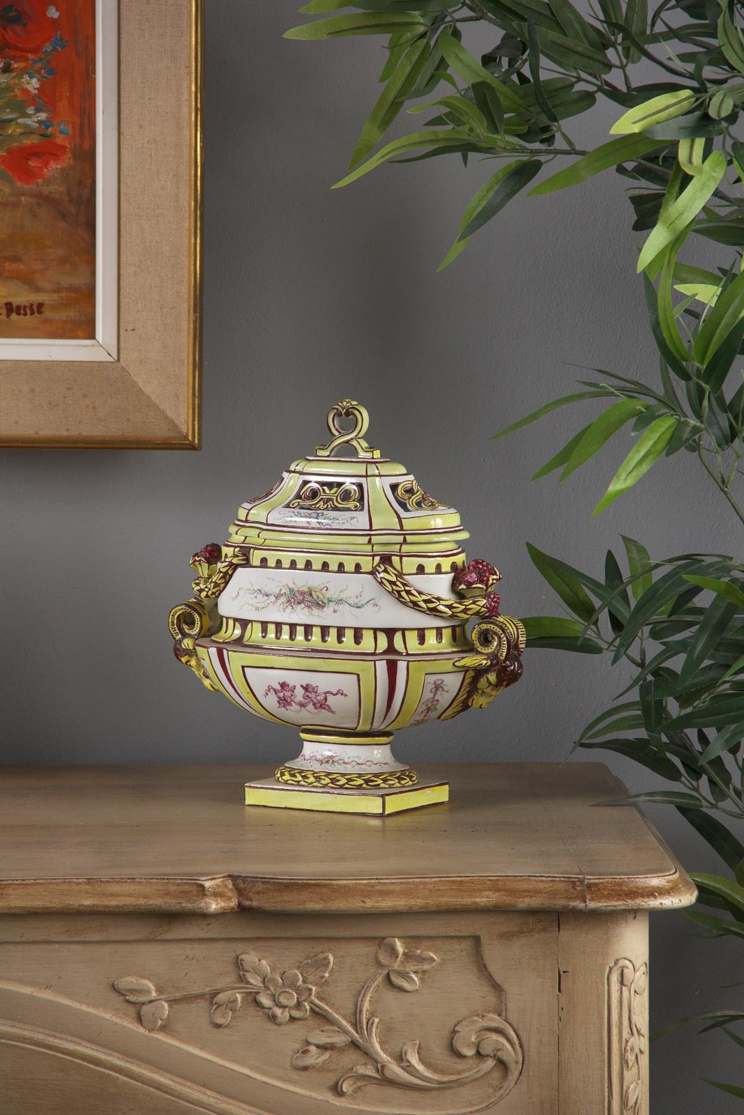 A colorful glazed Vieux Paris ceramic urn from the early 1900s. Wide ceramic form set up on a pedestal and a removable lid with decorated open work for potpourri housing. Scrolling ram's head handles on either side glazed in yellow with burgundy