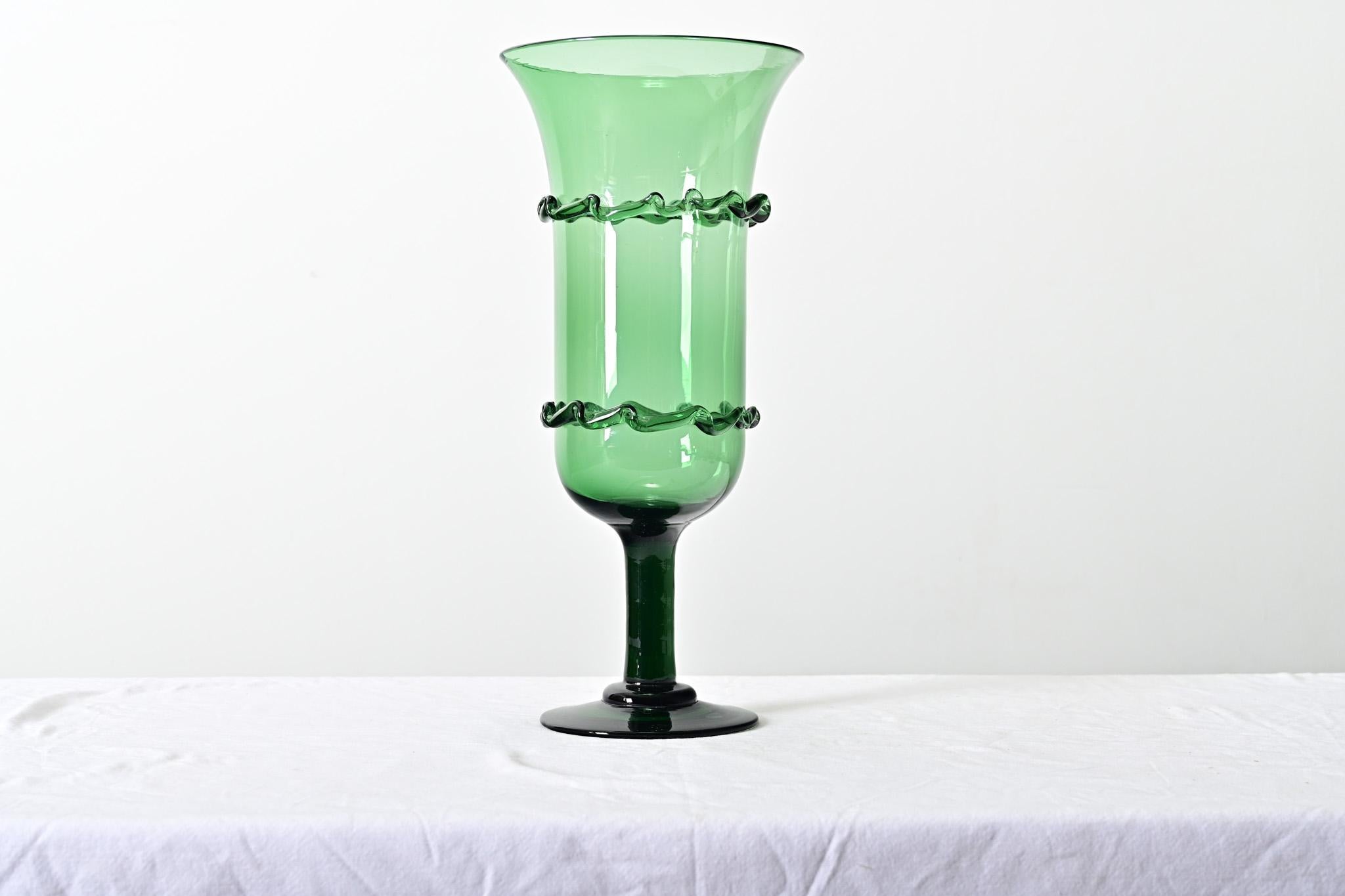 French vintage 20th century handmade, emerald green footed vase. The cylindrical “bowl” of the vessel has straight, tall walls–very similar to a celery vase of the late 19th/early 20th centuries–flaring out to a broad lip at the top. This example