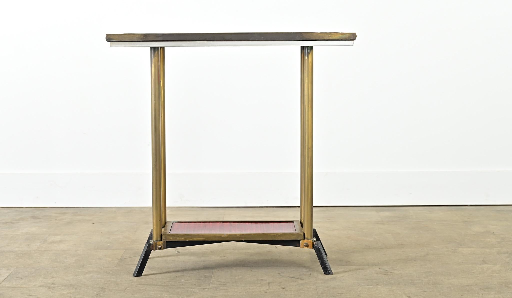 This modern, vintage 20th century occasional table has an Art Deco profile in its angular brass frame of two tiers of faux red mahogany veneer. The thick upper surface is trimmed in brass with two studs on each end (an industrial touch), framing the