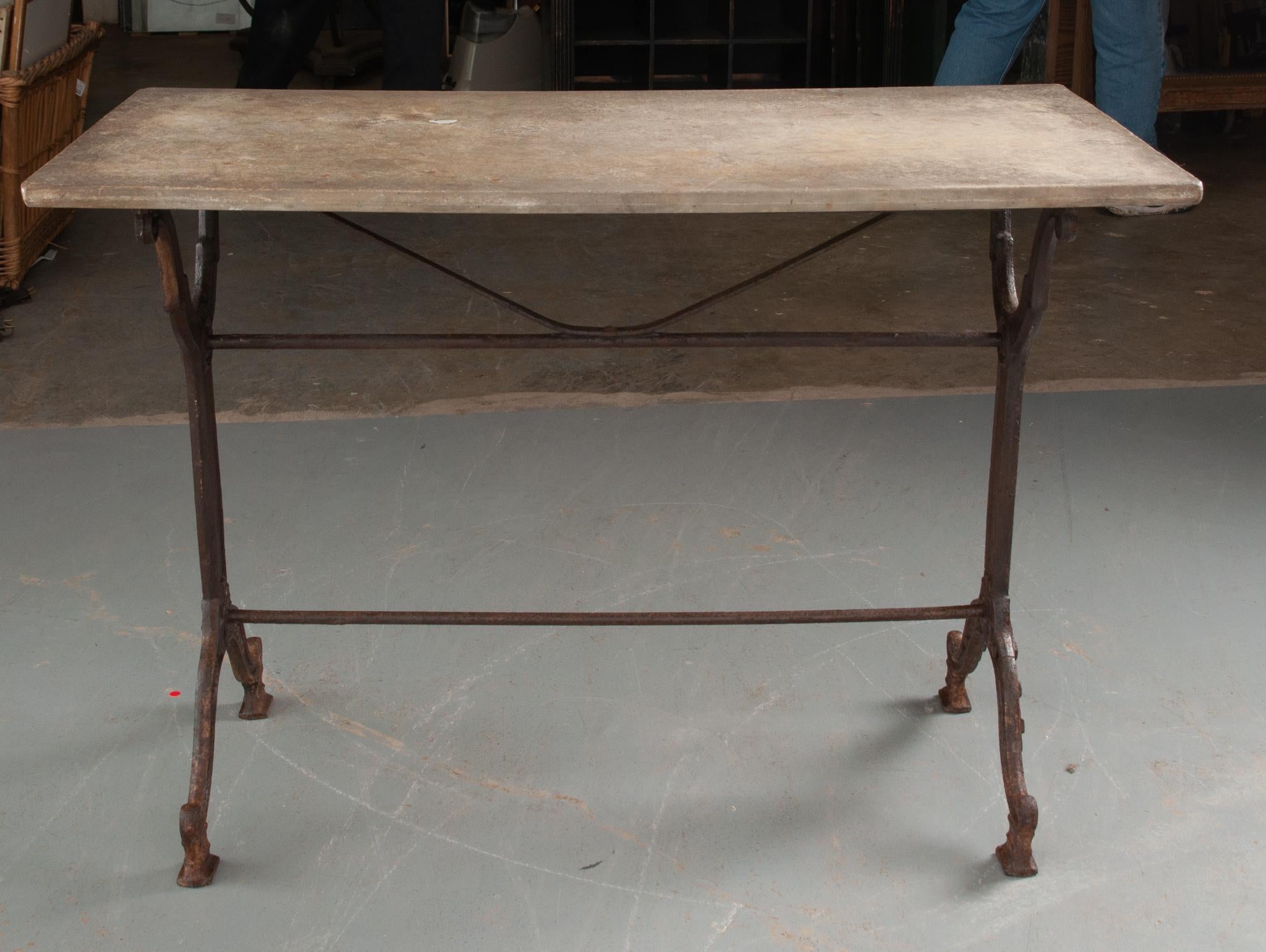 This rustic concrete top garden table was made in France. Weathered over the years, the top is in antique condition. The cast iron base is classically styled, with fashioned upright supports, linked by two iron stretcher braces. The worn iron