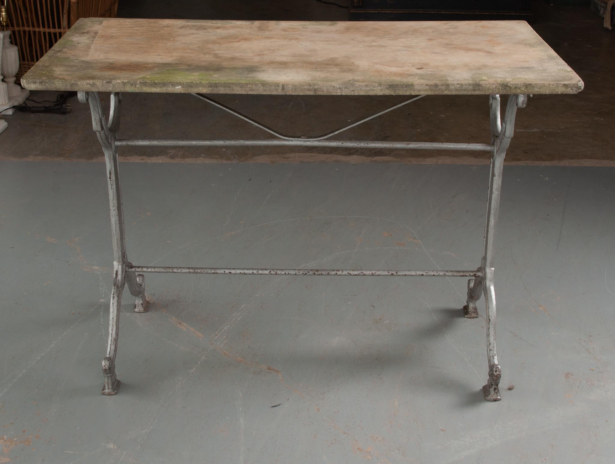 This rustic concrete top garden table was made in France. Weathered over the years, the top is in antique condition. The cast iron base is classically styled, with fashioned upright supports, linked by two iron stretcher braces. The worn iron