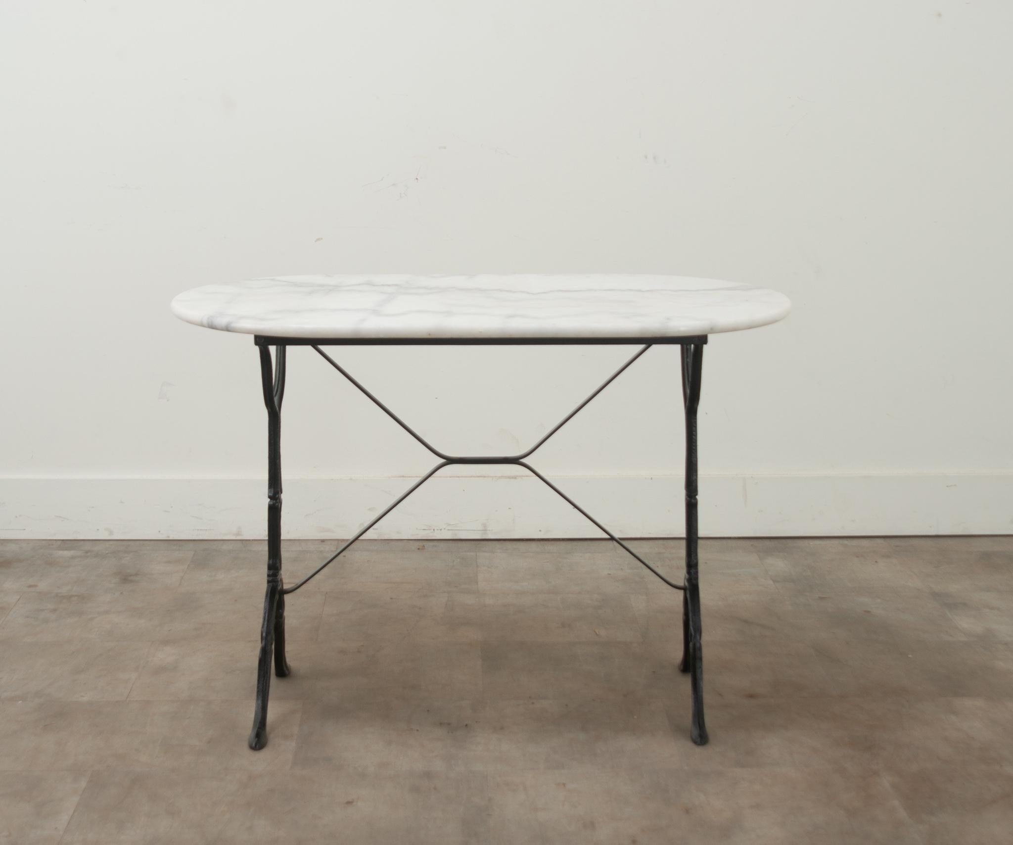 A classically styled French bistro table featuring a white capsule-shaped marble top over a cast iron base. This petite dining table shows wear consistent with age and use. Be sure to view the detailed images to see the current condition. 