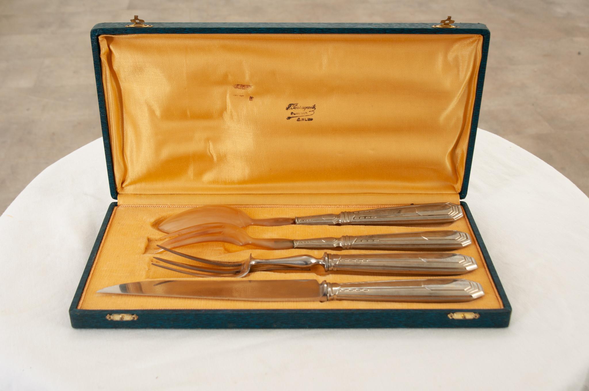 Encased in navy blue leather and protected by gold velvet, this set of 4 serving utensils includes a carving fork and knife and a salad serving fork and spoon. The carving knife has the maker's initials and the word “inoxydable” which means